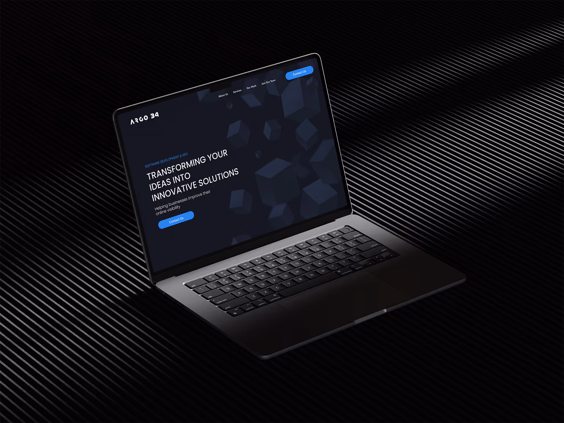 A sleek, dark laptop is angled on a dark, ridged surface, displaying a website for "ARGO 34." The screen shows "TRANSFORMING YOUR IDEAS INTO INNOVATIVE SOLUTIONS" against an abstract dark blue background.