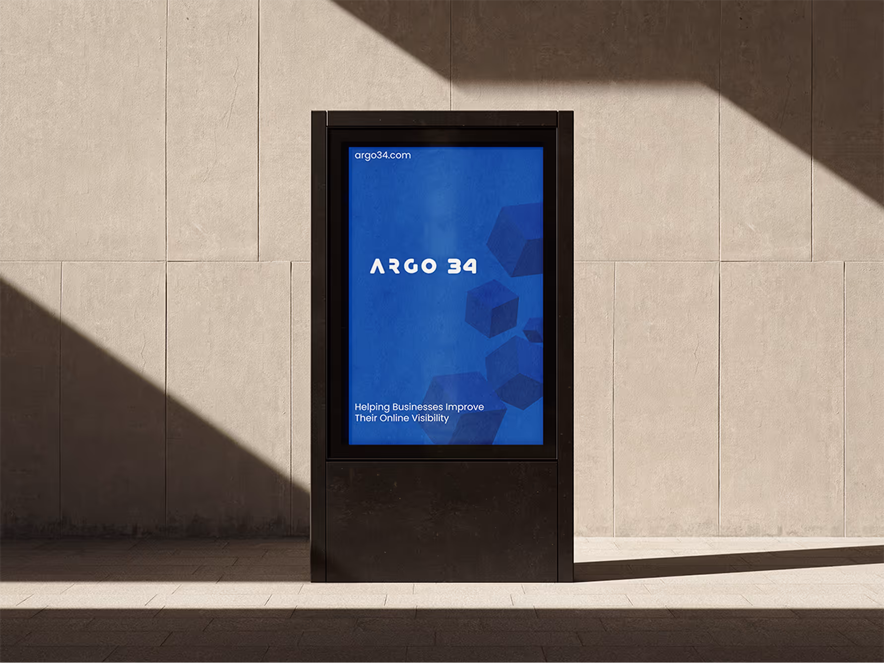 A tall, dark digital display sign with "ARGO 34" logo and website "argo34.com" is set against a light concrete wall. The screen shows a blue background with abstract cubes and the text "Helping Businesses Improve Their Online Visibility."