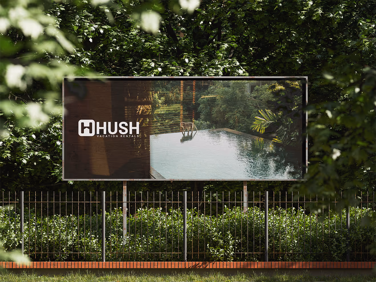 A horizontal billboard advertising "HHUSH VACATION RENTALS" is visible through green foliage and a metal fence. The billboard displays an image of an infinity pool surrounded by lush jungle, with a deer standing near the water's edge.