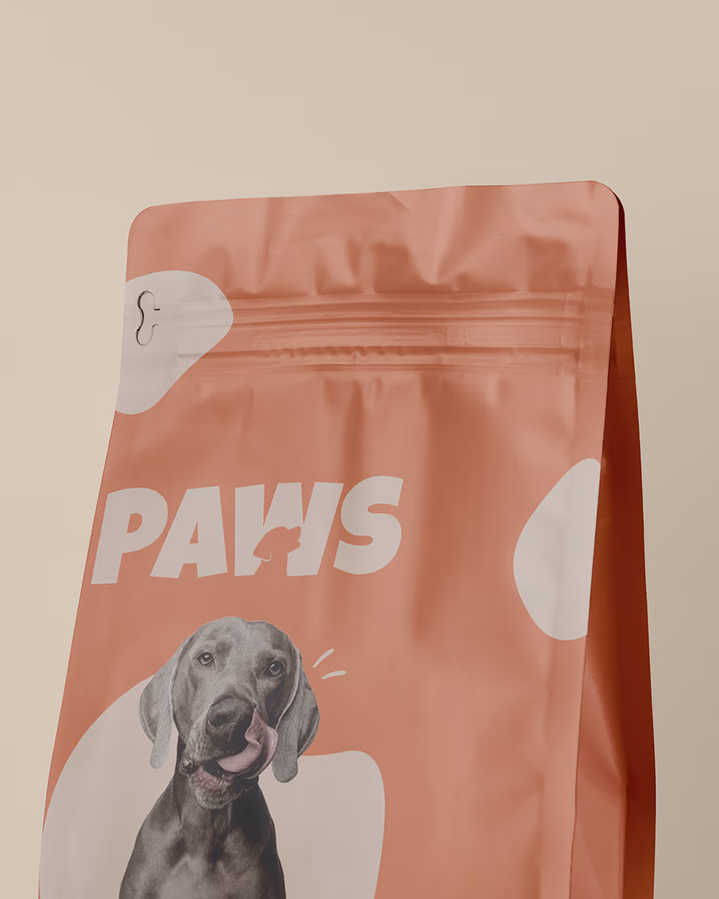 A close-up of a pet food bag with "PAWS" logo and a paw print for the 'W'. The bag is peach-colored, featuring a gray dog licking its snout.