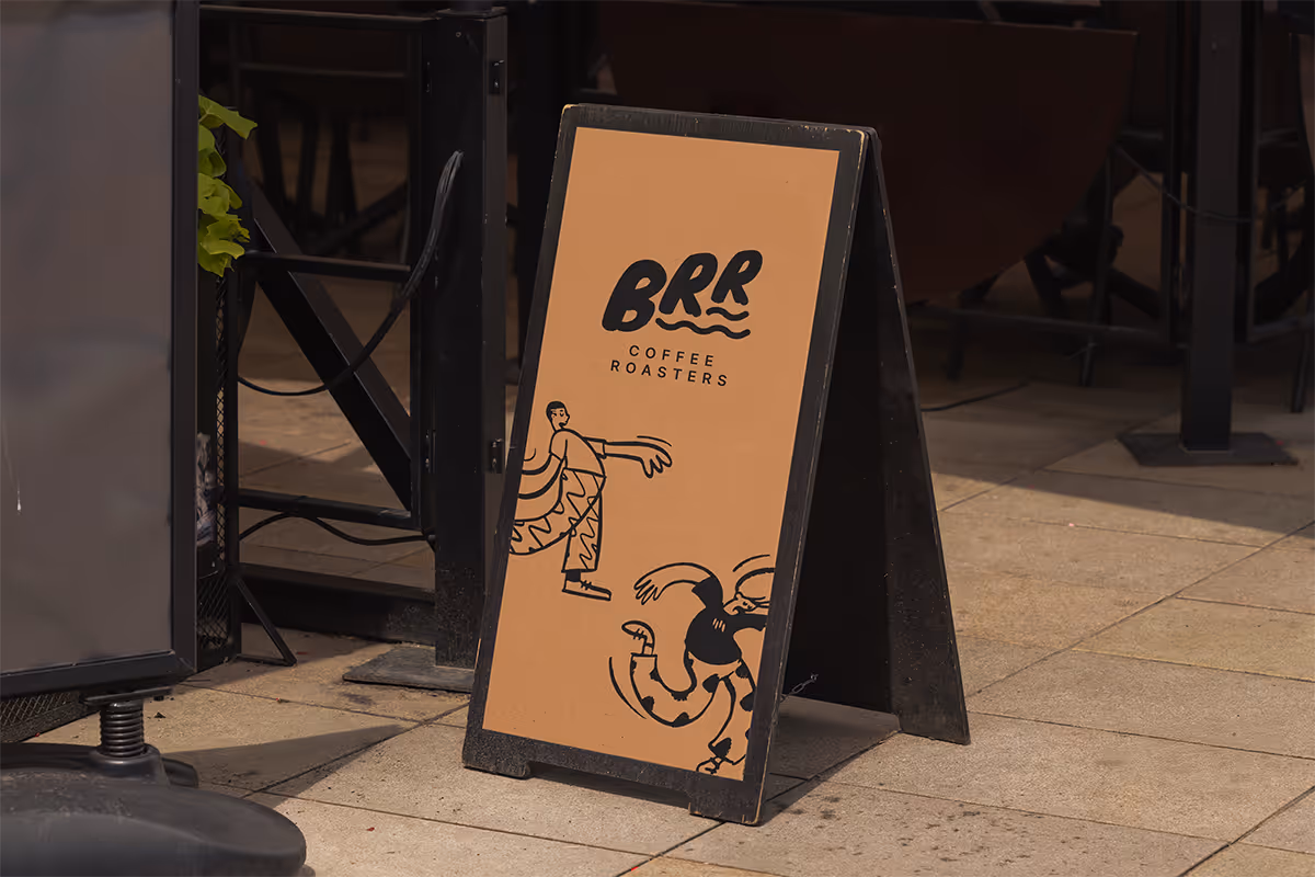 A-frame sign for "BRR COFFEE ROASTERS" on a sidewalk. The sign is dark brown with black text and abstract illustrations.
