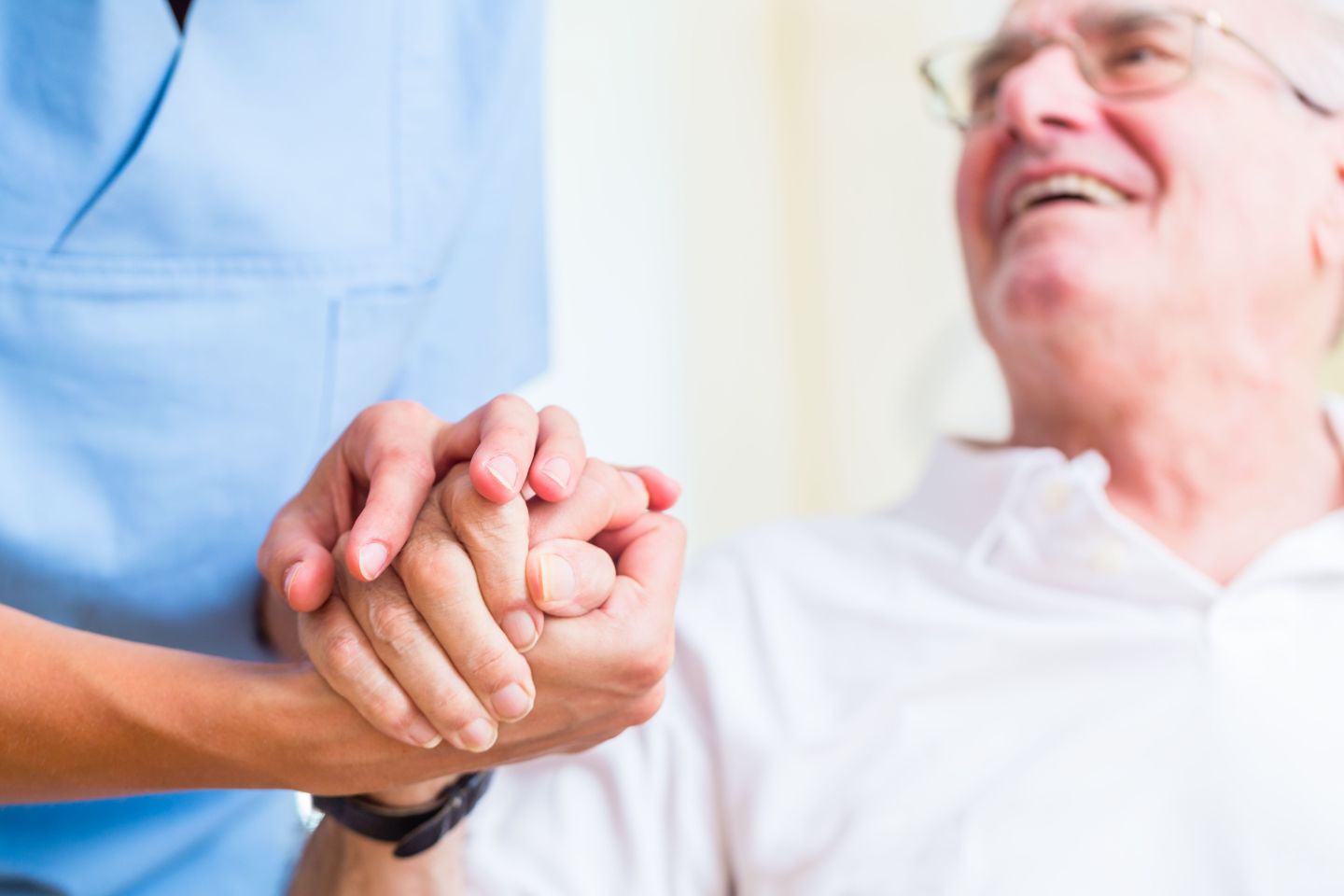 Älterer lächelnder Herr hält die Hand einer Pflegekraft