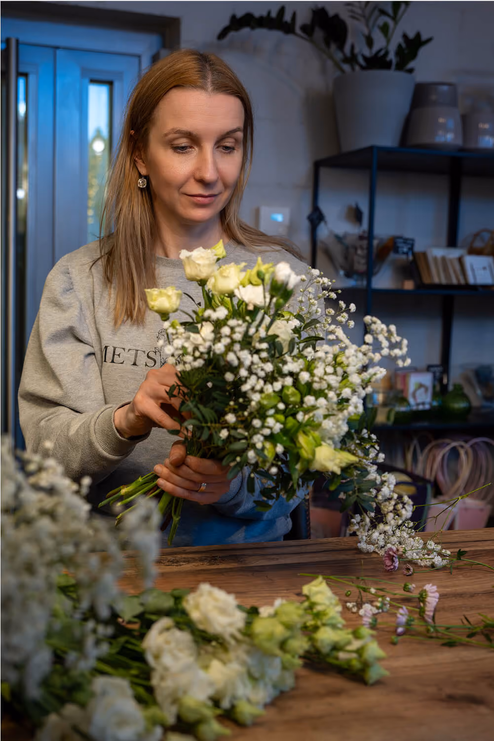 Florist lillepoes valmistamas valget roosikimpu ja kipslilli