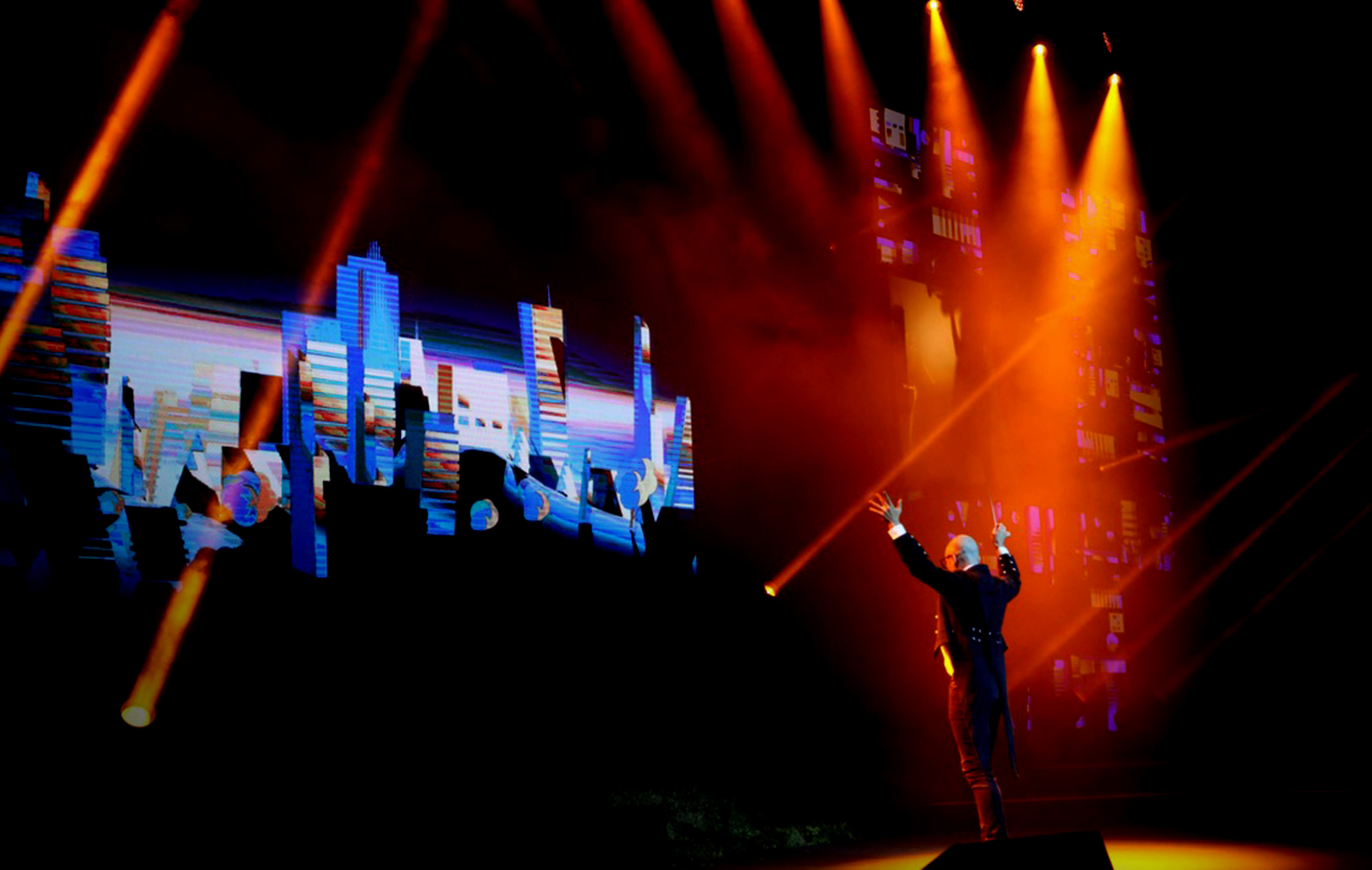 A conductor on stage with red lights and screens