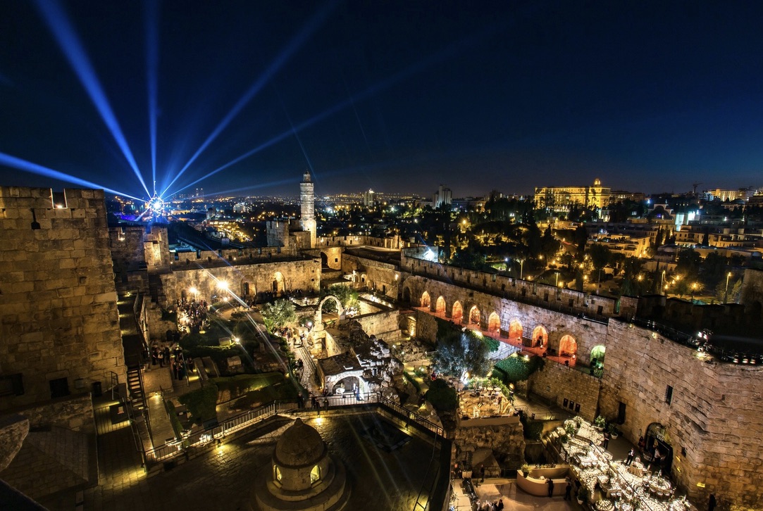 An illuminated wedding celebration at the historic Tower of David in Jerusalem, featuring dramatic lighting beams and the ancient stone architecture glowing against the night sky.