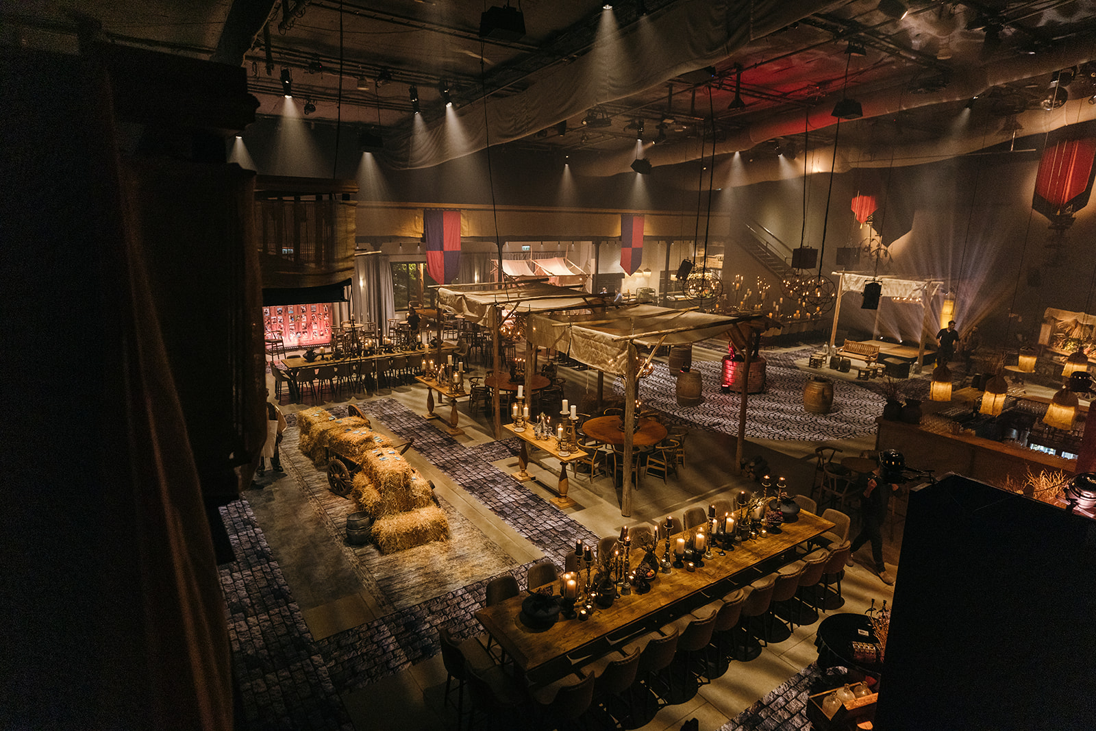 A medieval-themed indoor venue for an Israel bar mitzvah celebration, featuring wooden market stalls, hay bales, lanterns, and dramatic ambient lighting creating a warm, immersive atmosphere.