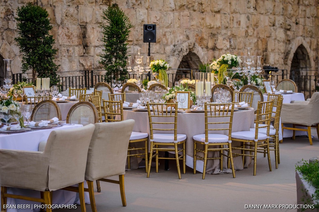 Luxurious round and rectangular tables arranged in front of ancient wall.
