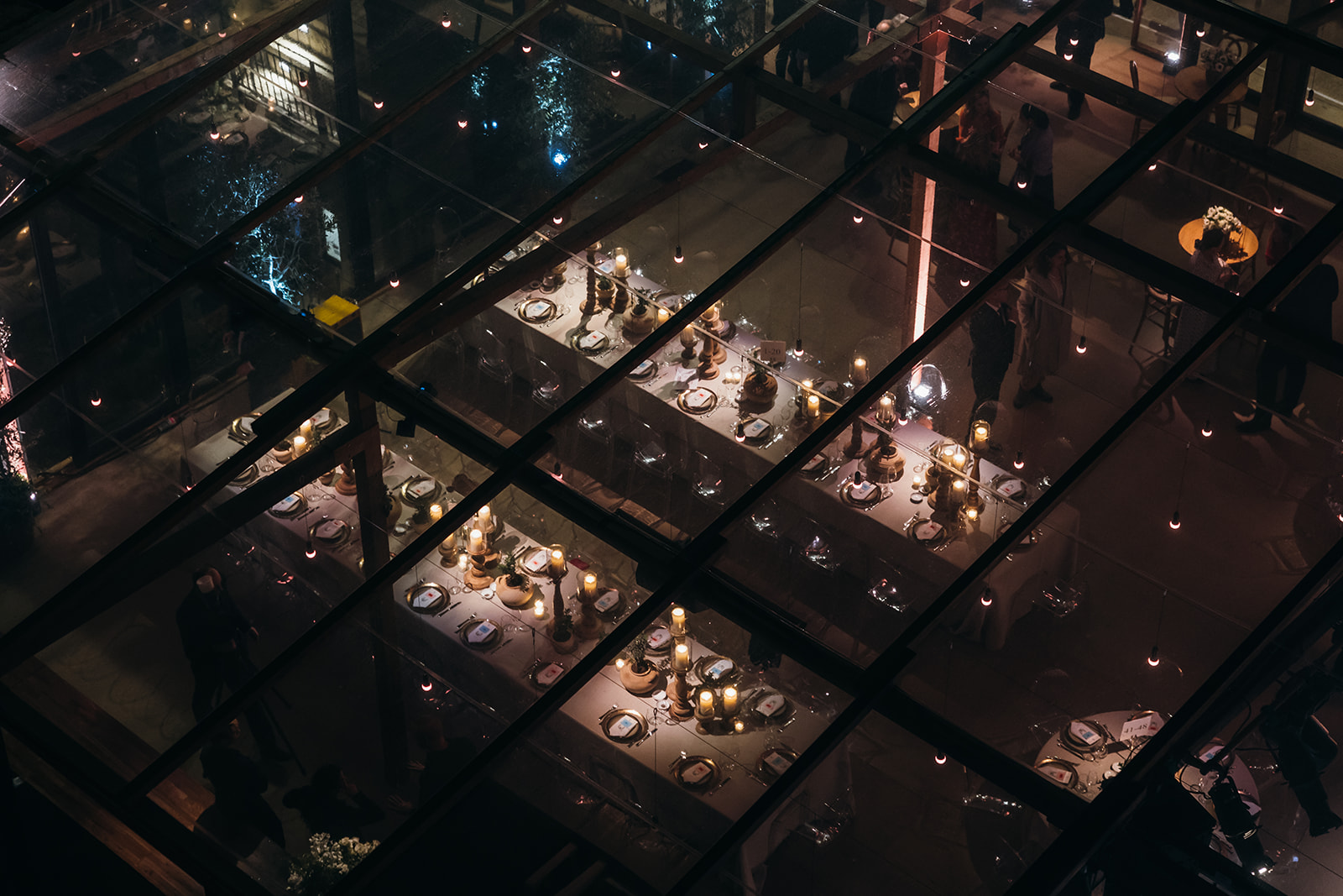 Decorated gala dinner table featuring tall candle holders and clay pots, all under a glass canopy with fairy lights.