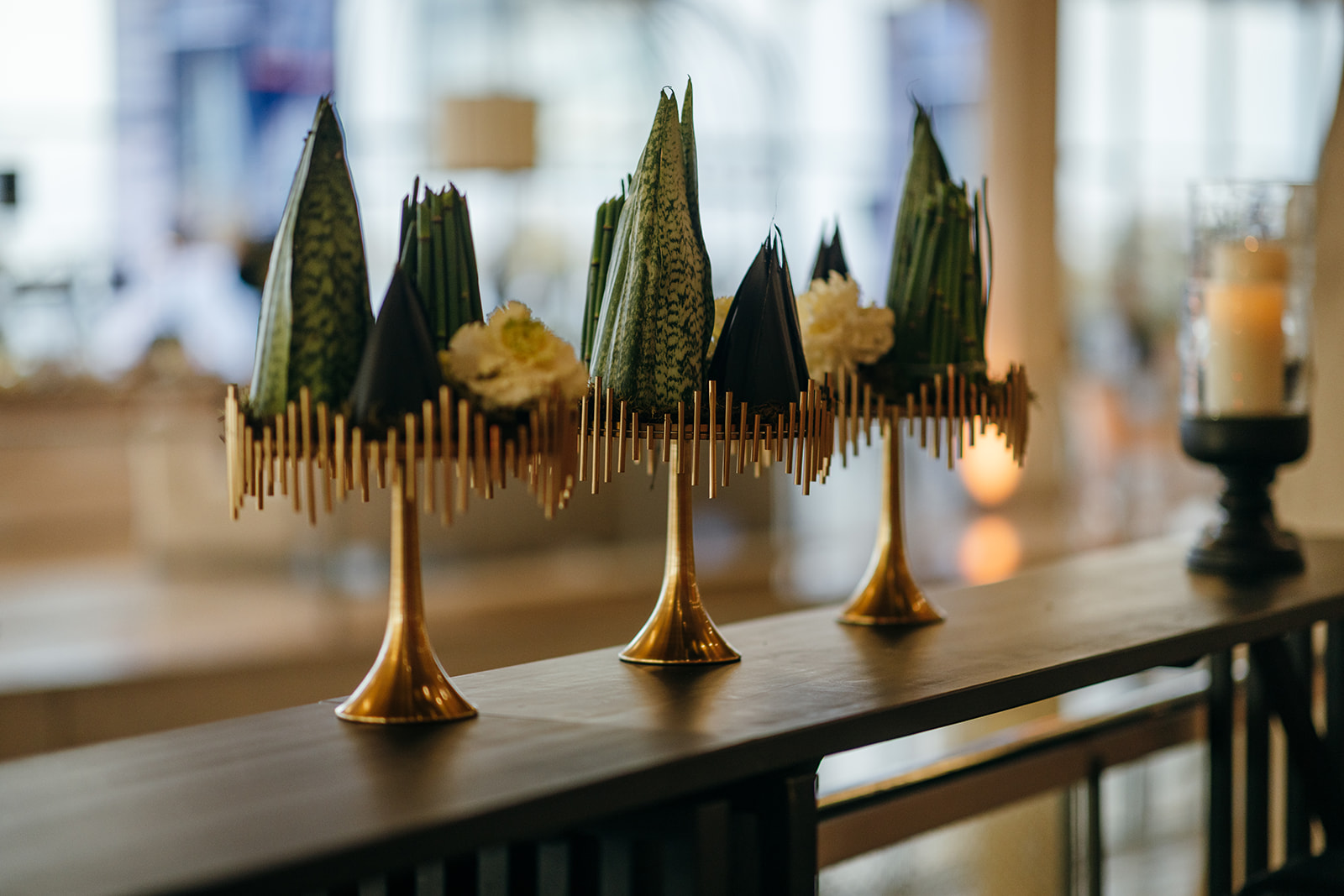 Close-up of modern green centerpiece arrangements on elegant gold stands.
