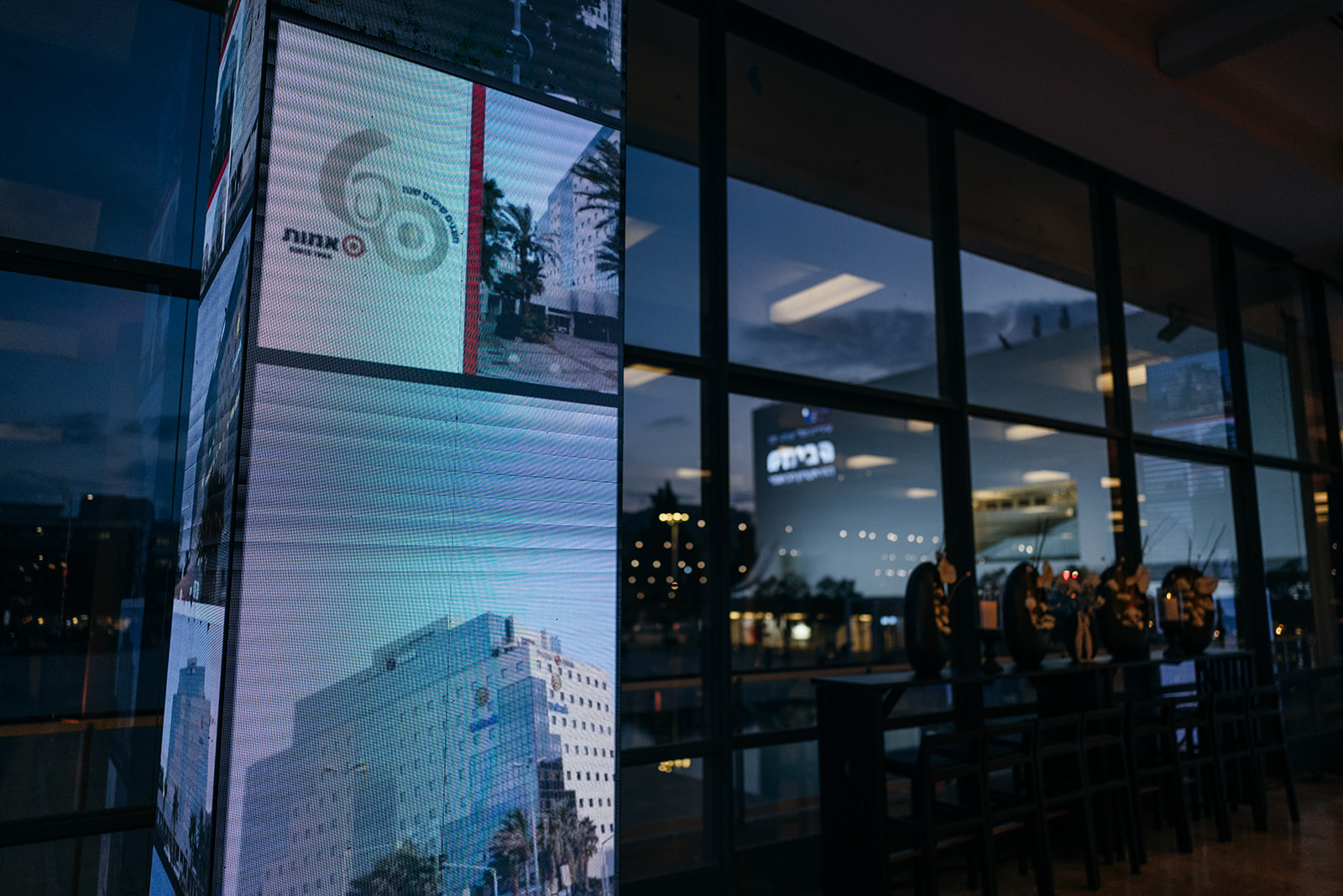 Evening view of the LED screen tower from inside the event hall, with city lights outside.