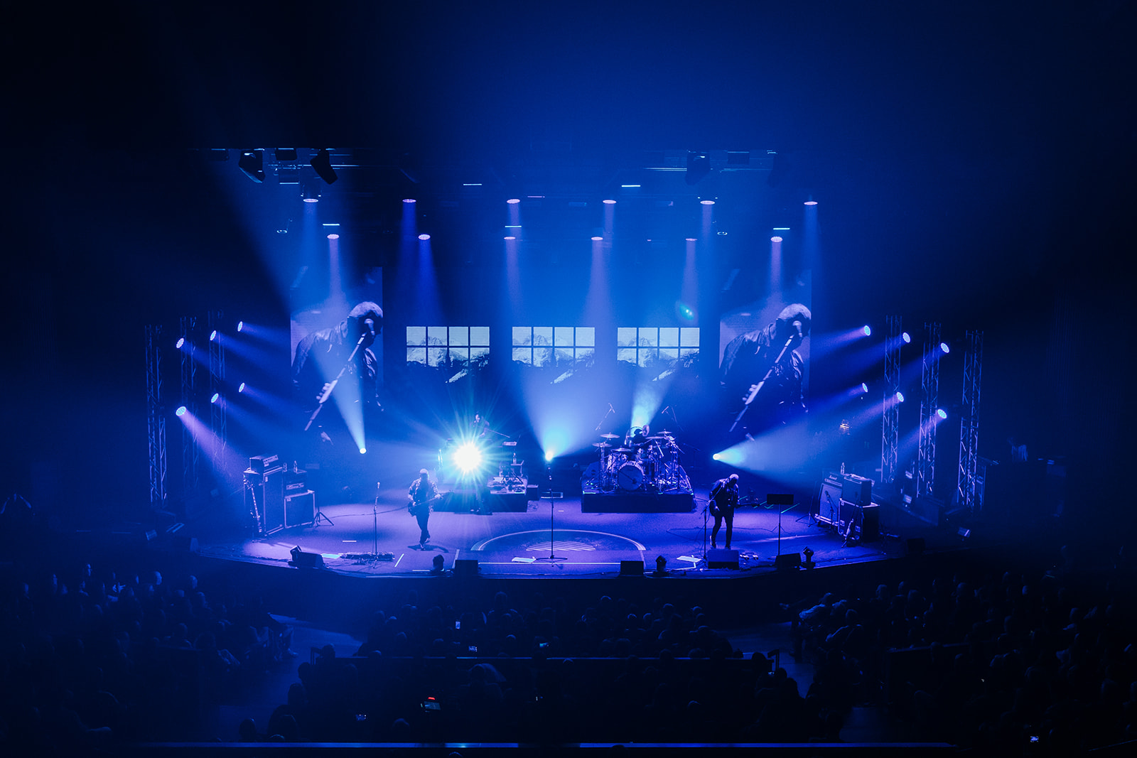 Full stage illuminated in blue lighting during a live band performance with visual effects.