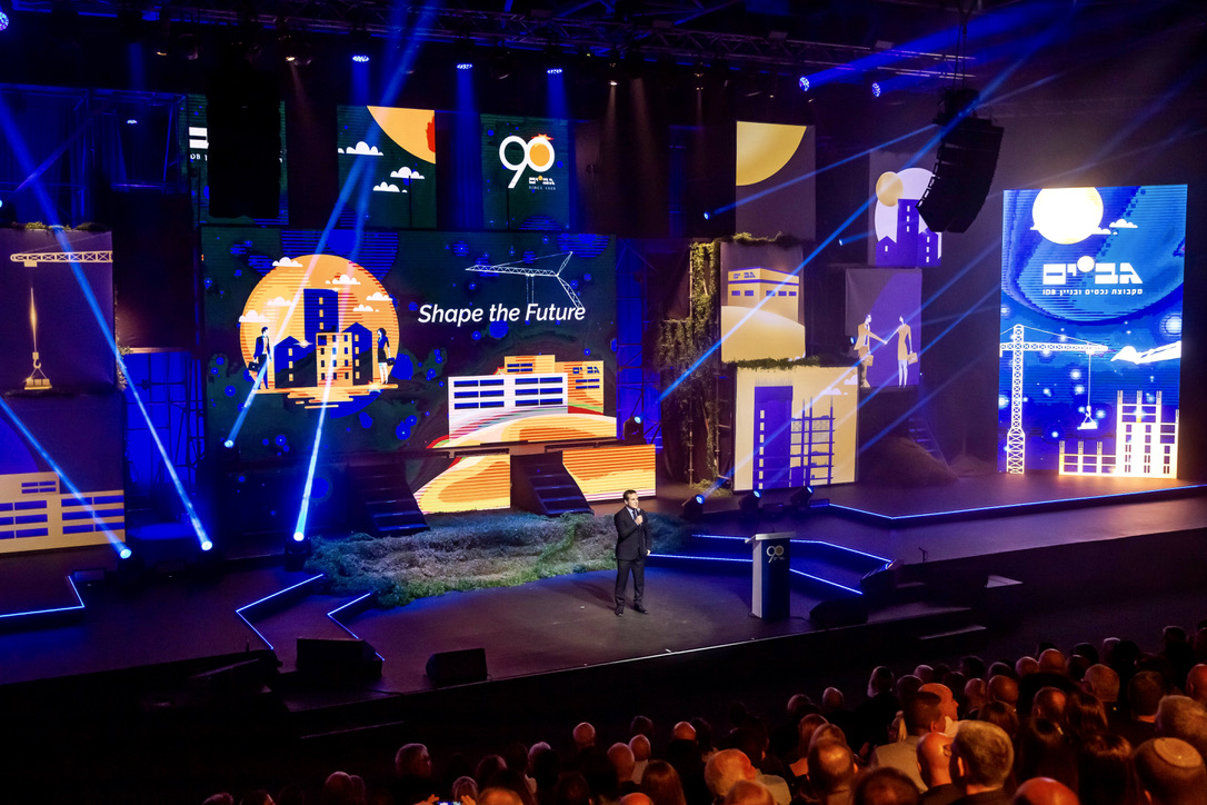 Keynote speaker on stage with “Shape the Future” theme at Gav-Yam 90th anniversary event.