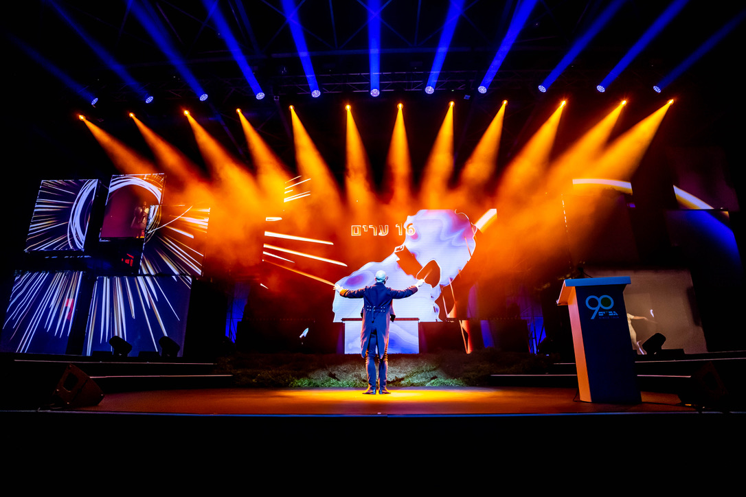 Performer on stage with vibrant lights and visuals at Gav-Yam 90th anniversary celebration.