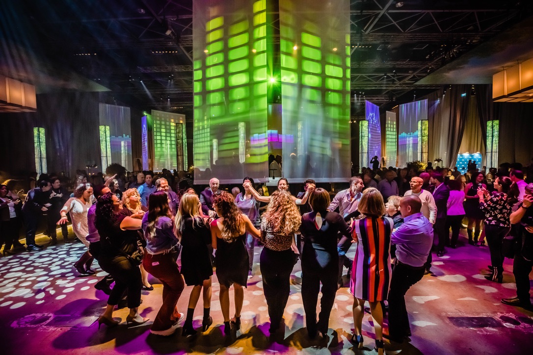 ``` A group of people dancing in a circle at a vibrant nightclub with colorful lights and digital projections.