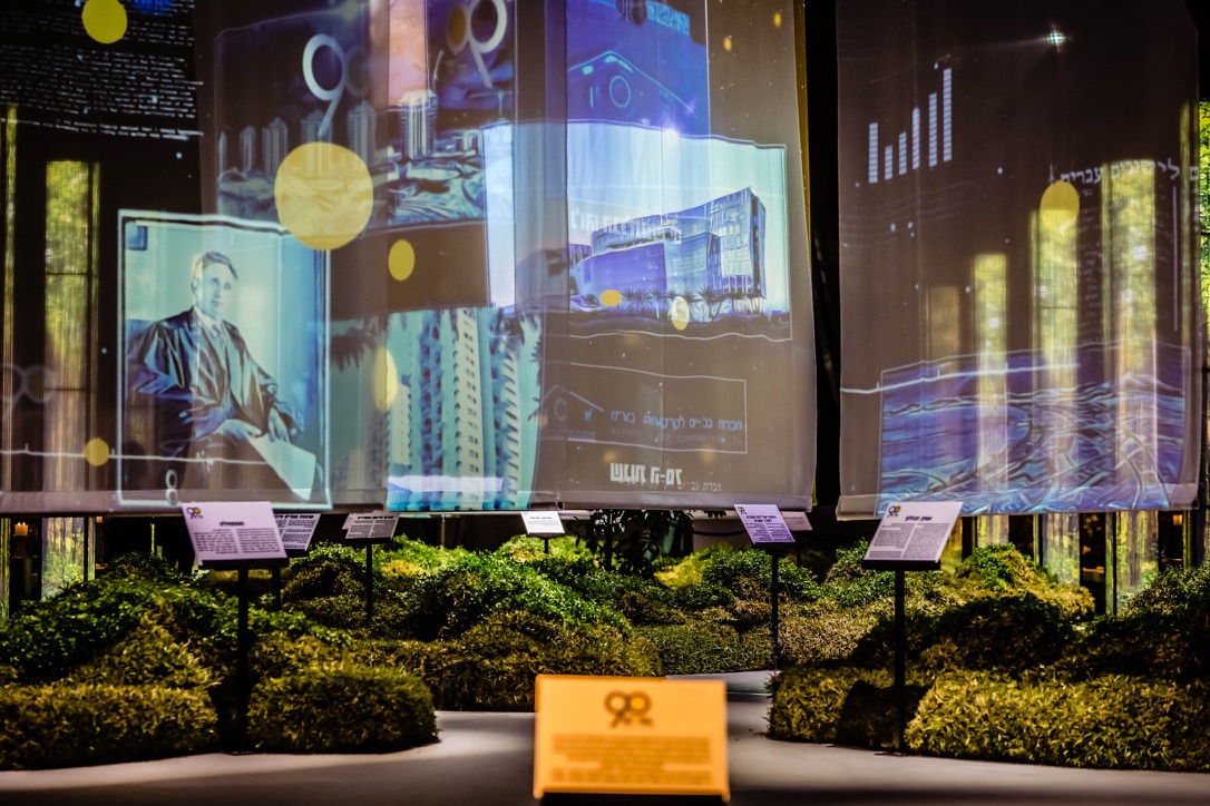 Historical projections and archival displays with greenery at Gav-Yam 90th anniversary celebration.