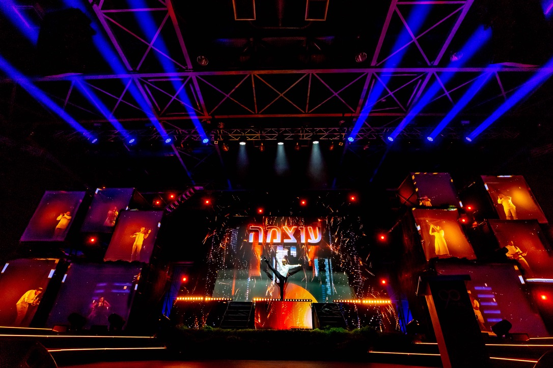 Dramatic stage performance with lights, dancers, and projections at Gav-Yam 90th anniversary celebration.