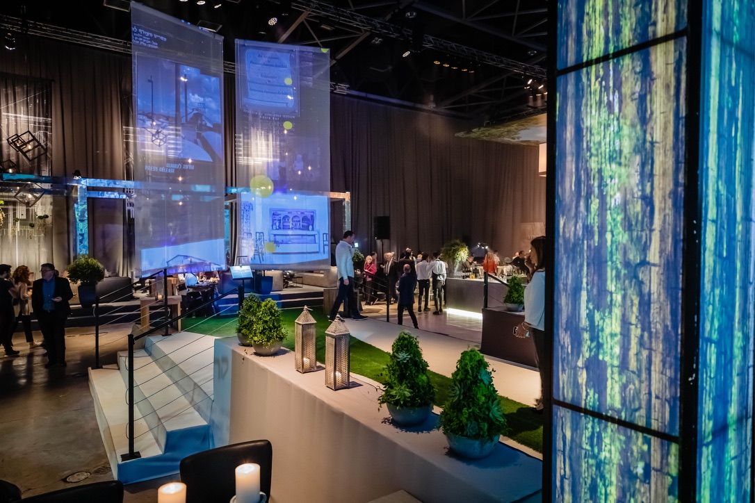 Decorative lounge setup with projections, greenery, and guests at Gav-Yam 90th anniversary celebration.