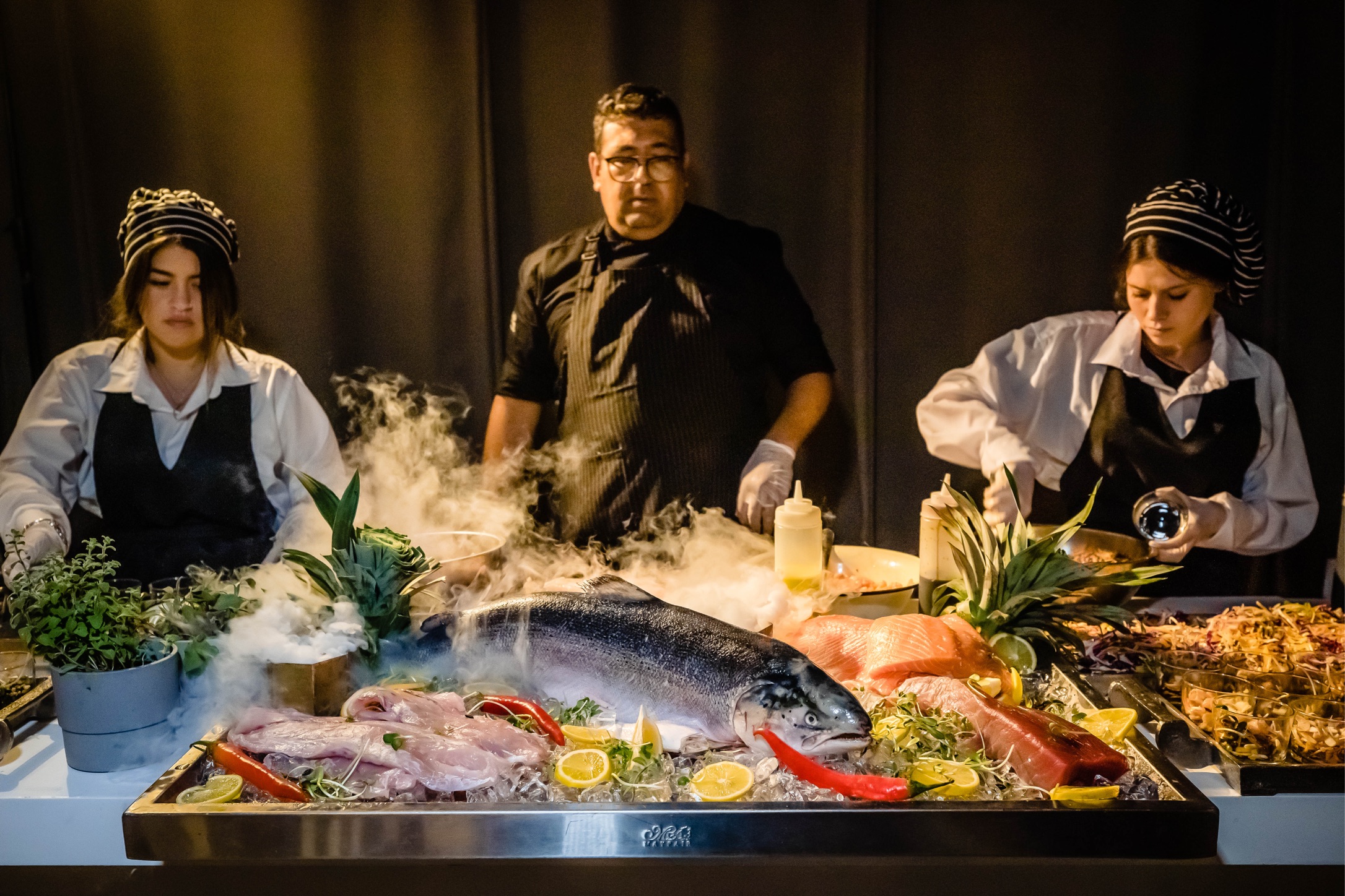 Chefs presenting fresh seafood display with salmon and gourmet dishes at Gav-Yam 90th anniversary event.