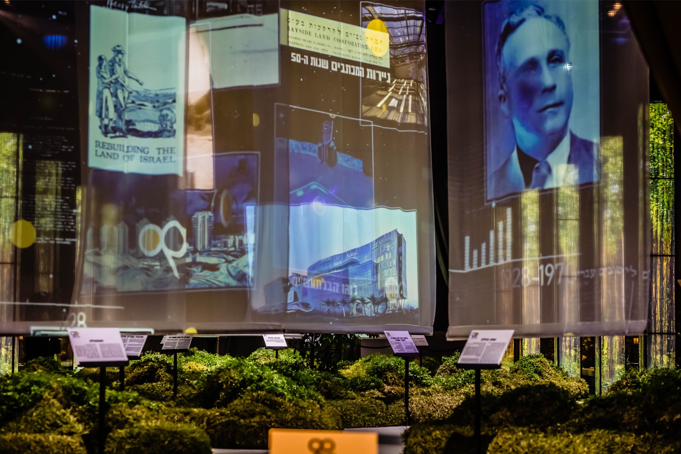Dramatic stage performance with lights, dancers, and projections at Gav-Yam 90th anniversary celebration.Historical photo and archival projections with greenery at Gav-Yam 90th anniversary celebration.