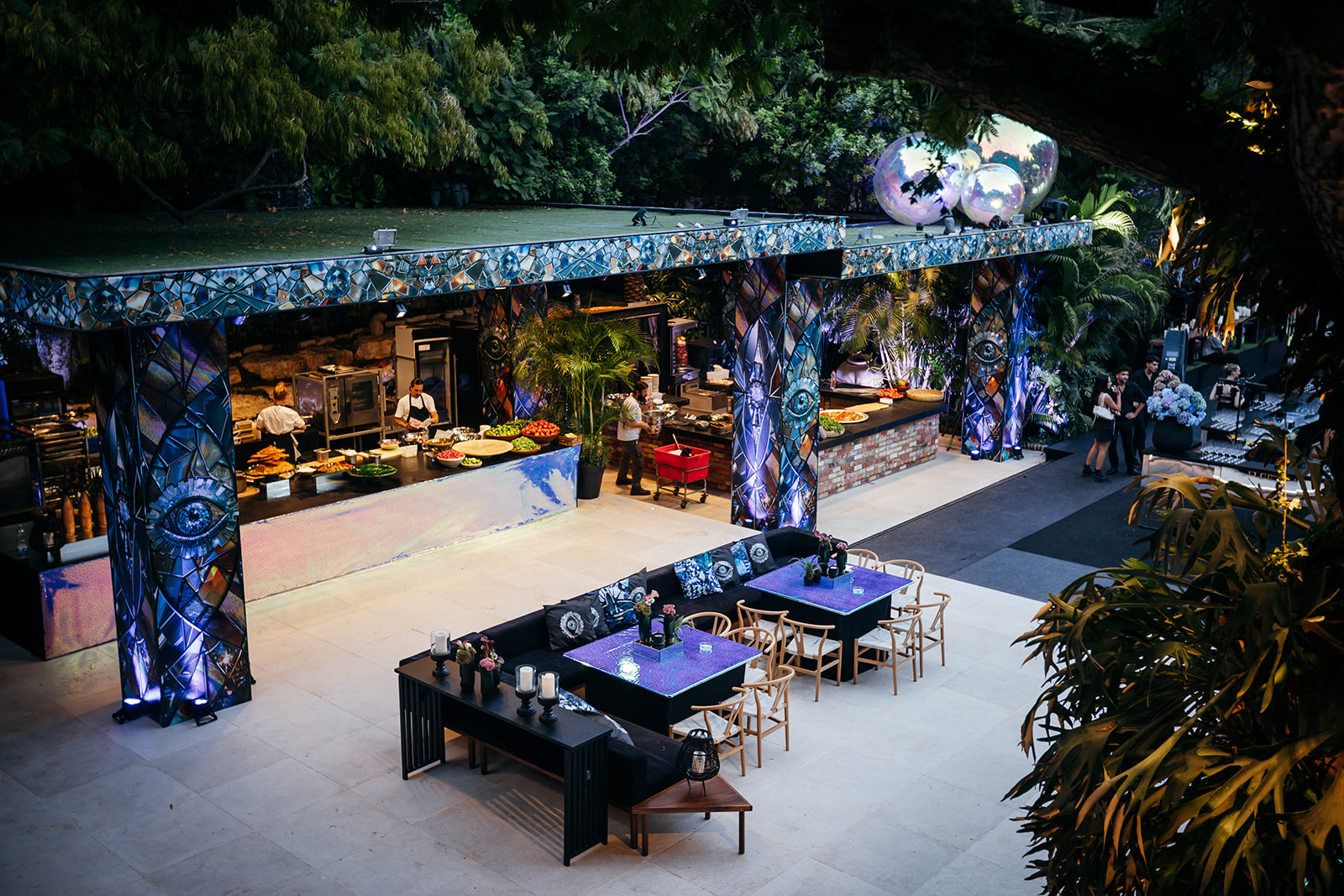 Stunning outdoor wedding venue and catering station in Israel, featuring unique mosaic columns and modern black and purple lounge seating. Luxury wedding decor.