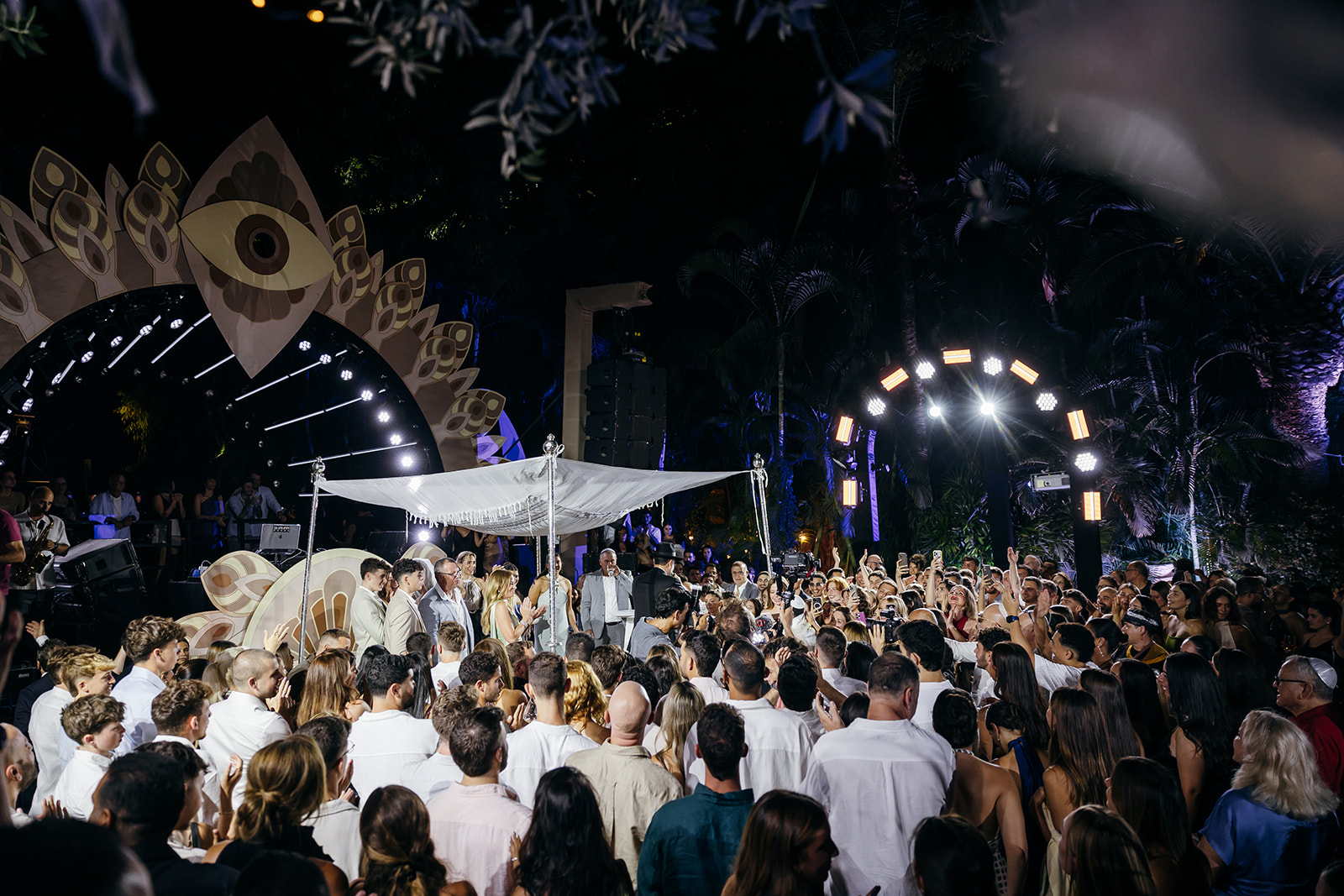 Emotional Jewish wedding chuppah ceremony at night in Israel, surrounded by family and friends with a unique stage and party lighting backdrop.
