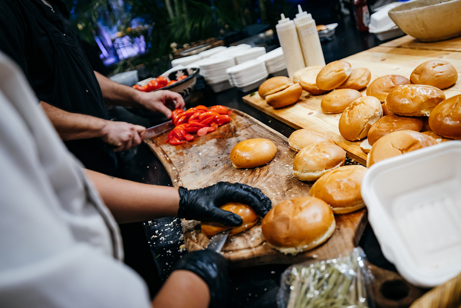 Close-up of fresh slider buns and sliced tomatoes being prepped by a caterer at a late-night wedding food station in Israel.