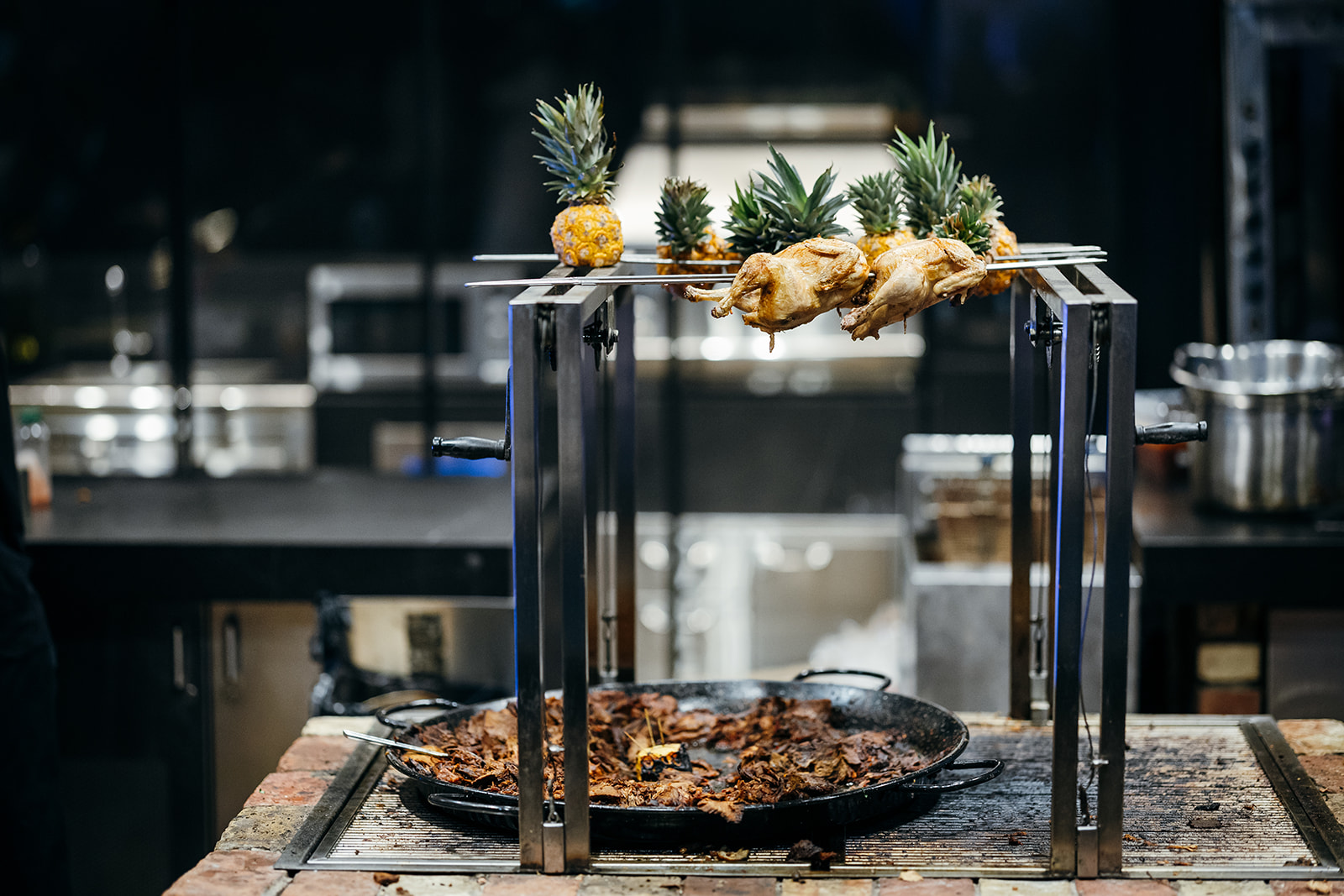 Gourmet live cooking station at a luxury Israeli wedding, featuring whole roasted chicken on a spit with pineapples and pan-seared meat. Unique wedding catering.