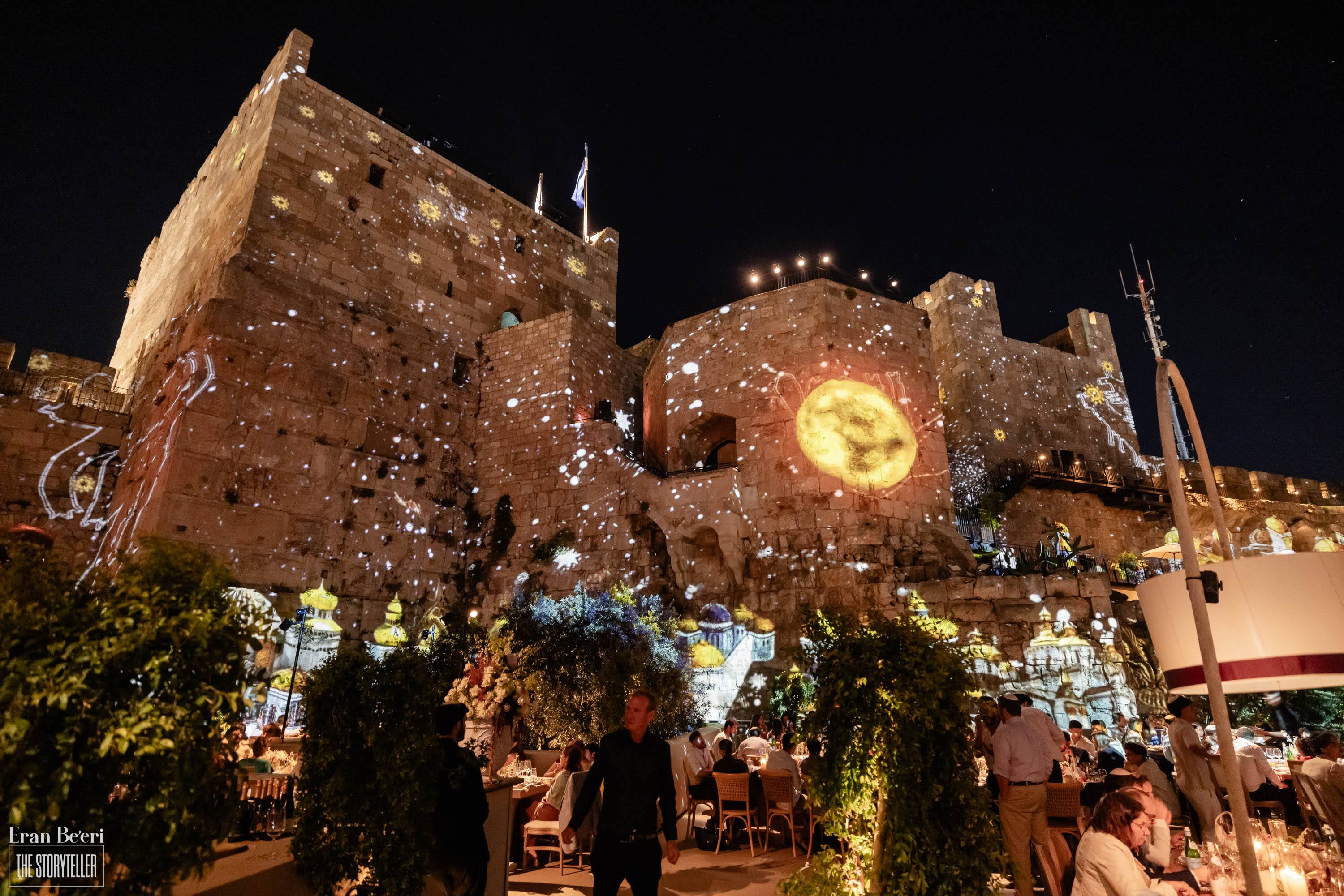 Artistic nighttime projections illuminating the historic Tower of David walls during an elegant wedding celebration in Jerusalem.