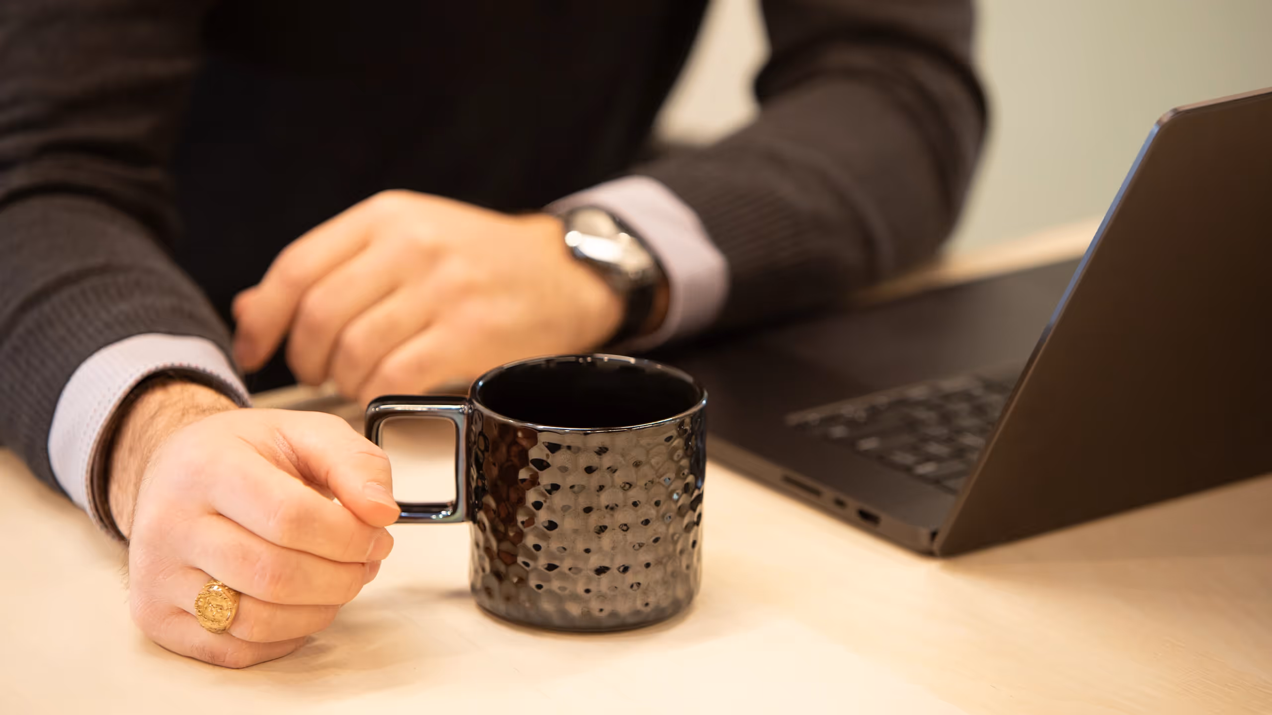 Close-up of a person holding a textured black coffee mug beside a laptop.