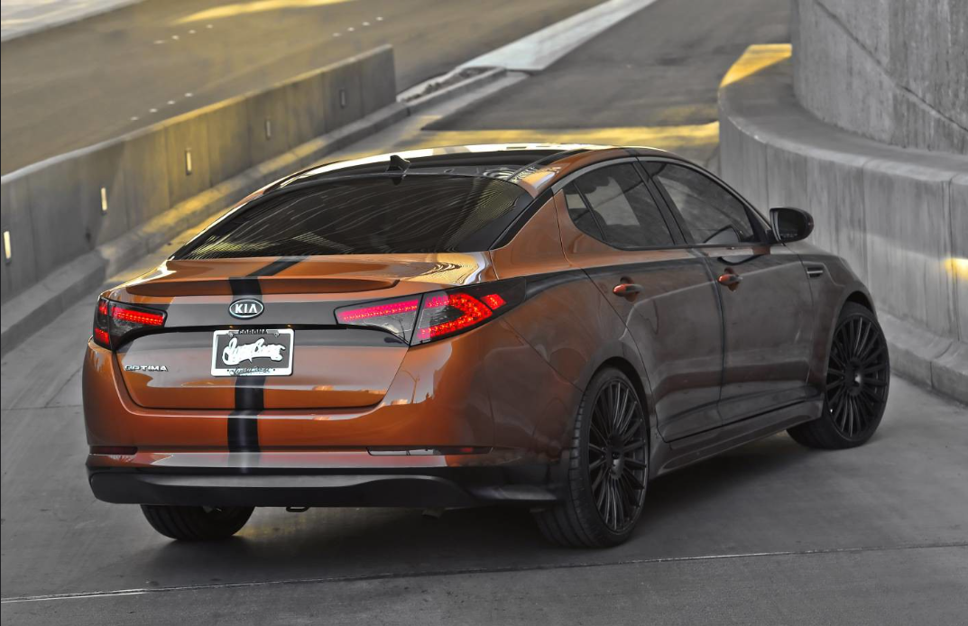 Image shows an orange and black Kia sedan with the brand’s previous logo on the trunk.
