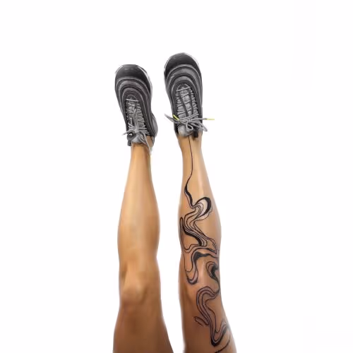 To ben oppe i luften set forfra, den ene med grå sneakers og den anden med en sort abstrakt tatovering langs benet.