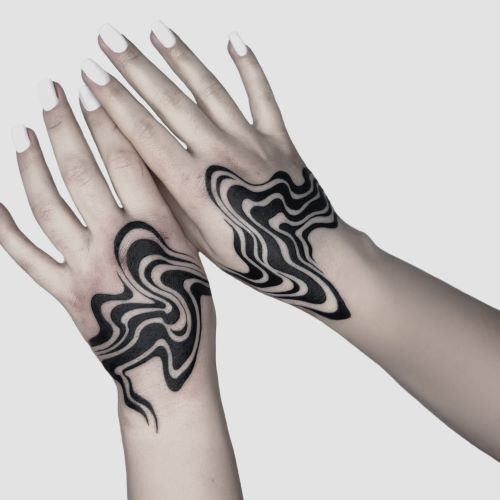 To hænder med sorte, bølgede, abstrakte tatoveringer på håndleddene mod en lys baggrund.