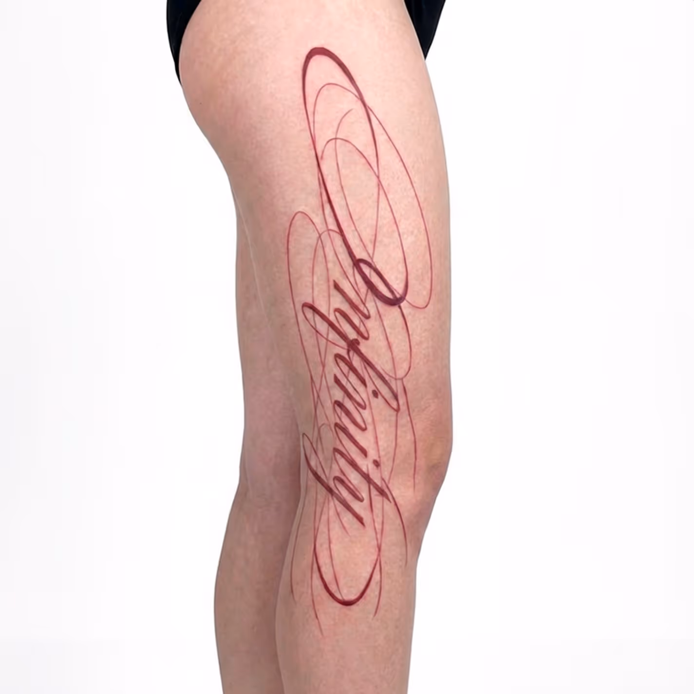 Tatovering på låret med ordet 'optimist' i udsmykket kursiv skrift.