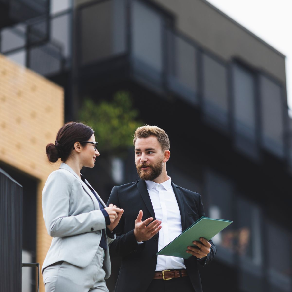 Two business professionals engaged in conversation on a city street, surrounded by urban scenery.