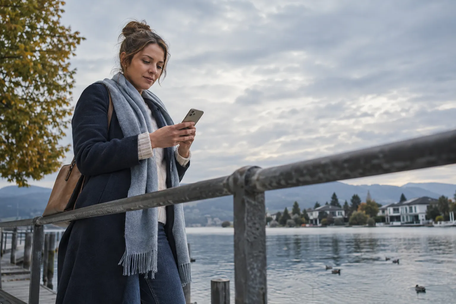 Eine Wohnungssuchende prüft am See Immobilienangebote auf dem Smartphone im weichen Wolkenlicht.