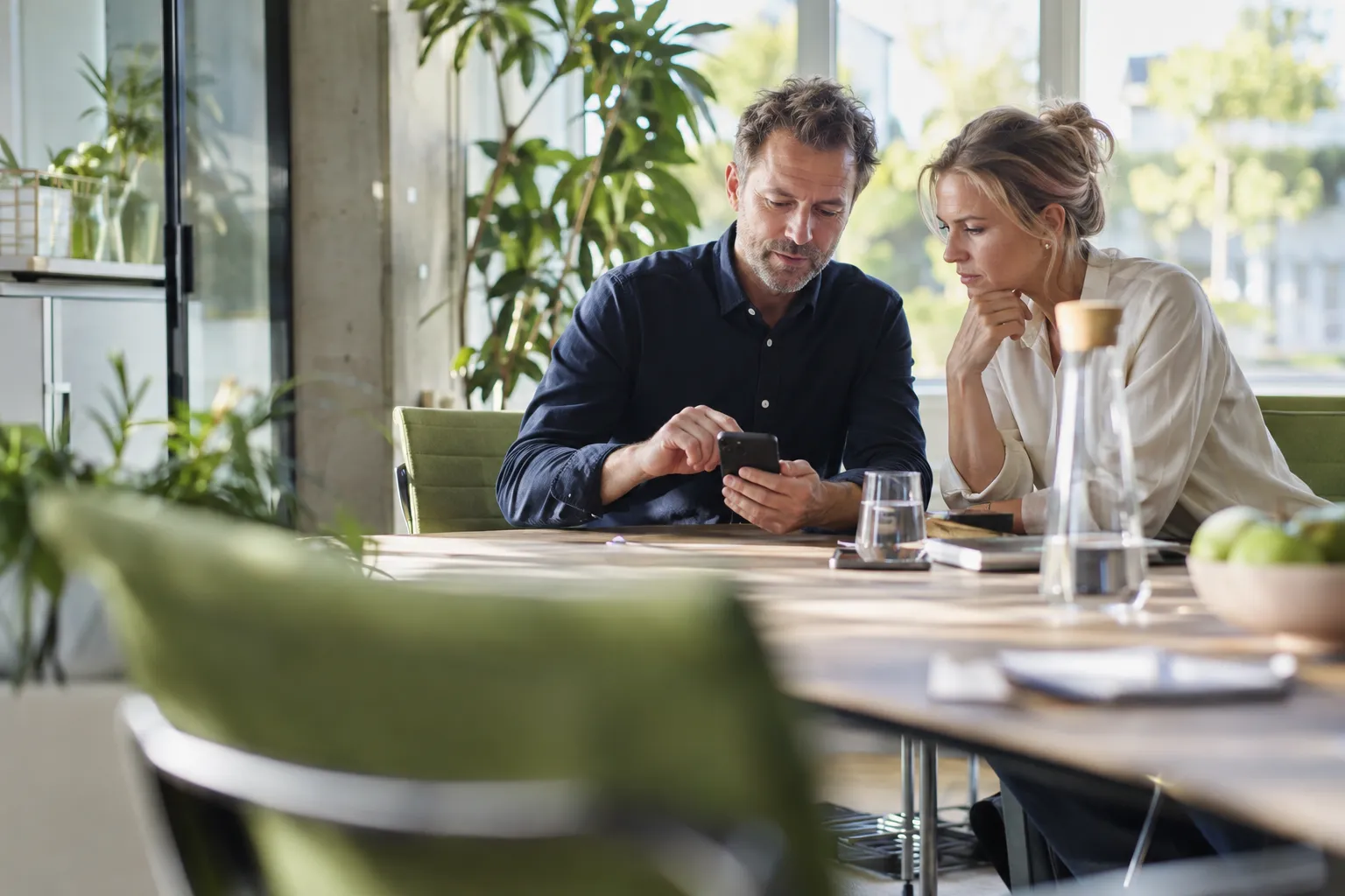 Zwei Einkäufer prüfen im hellen Besprechungsraum eine Webseite auf dem Smartphone und senden eine Beratungsanfrage.
