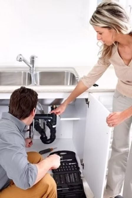 Two people looking under at the pipes under a kitchen sink.