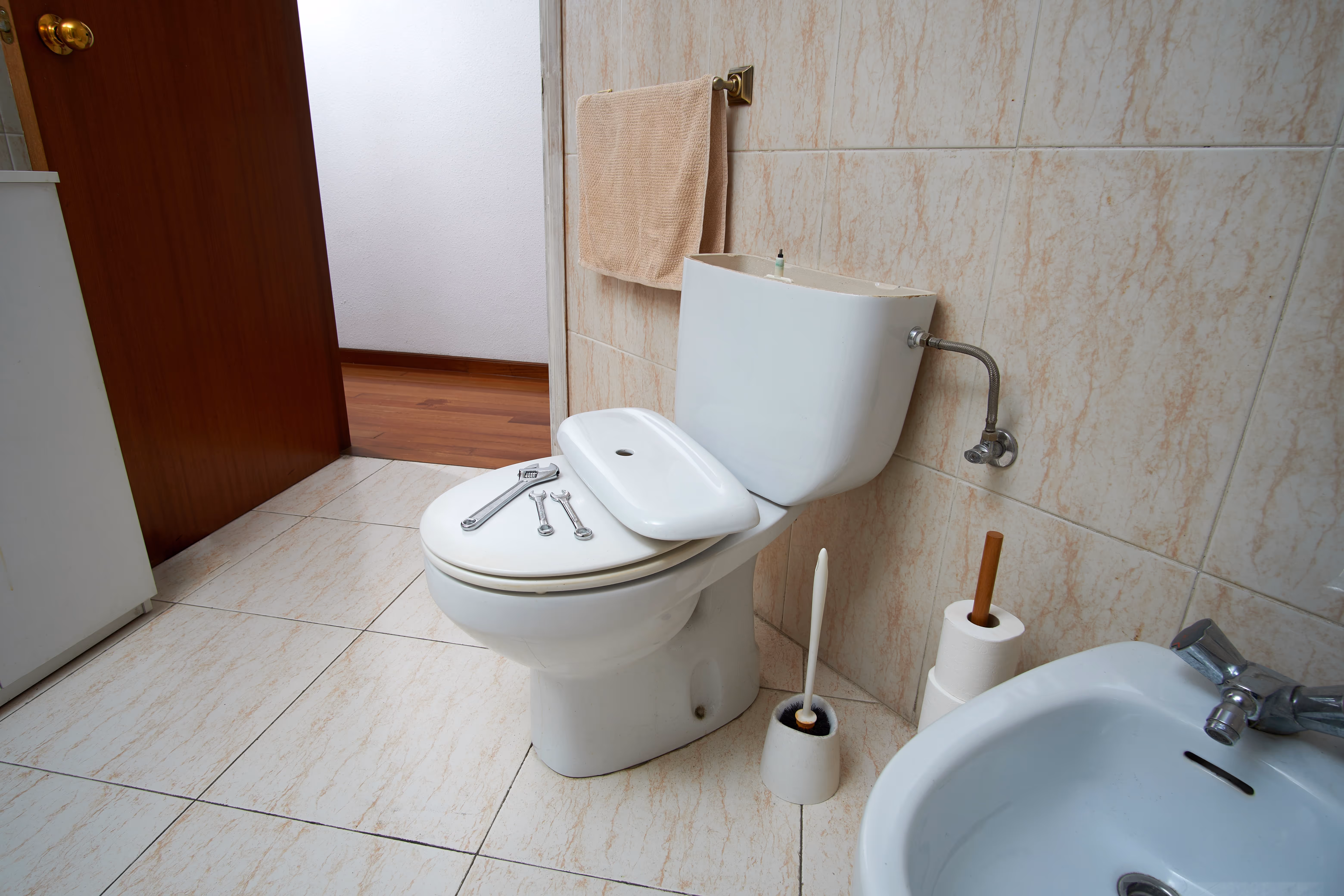 A toilet inside of a bathroom with tools on the seat as if it had been worked on.