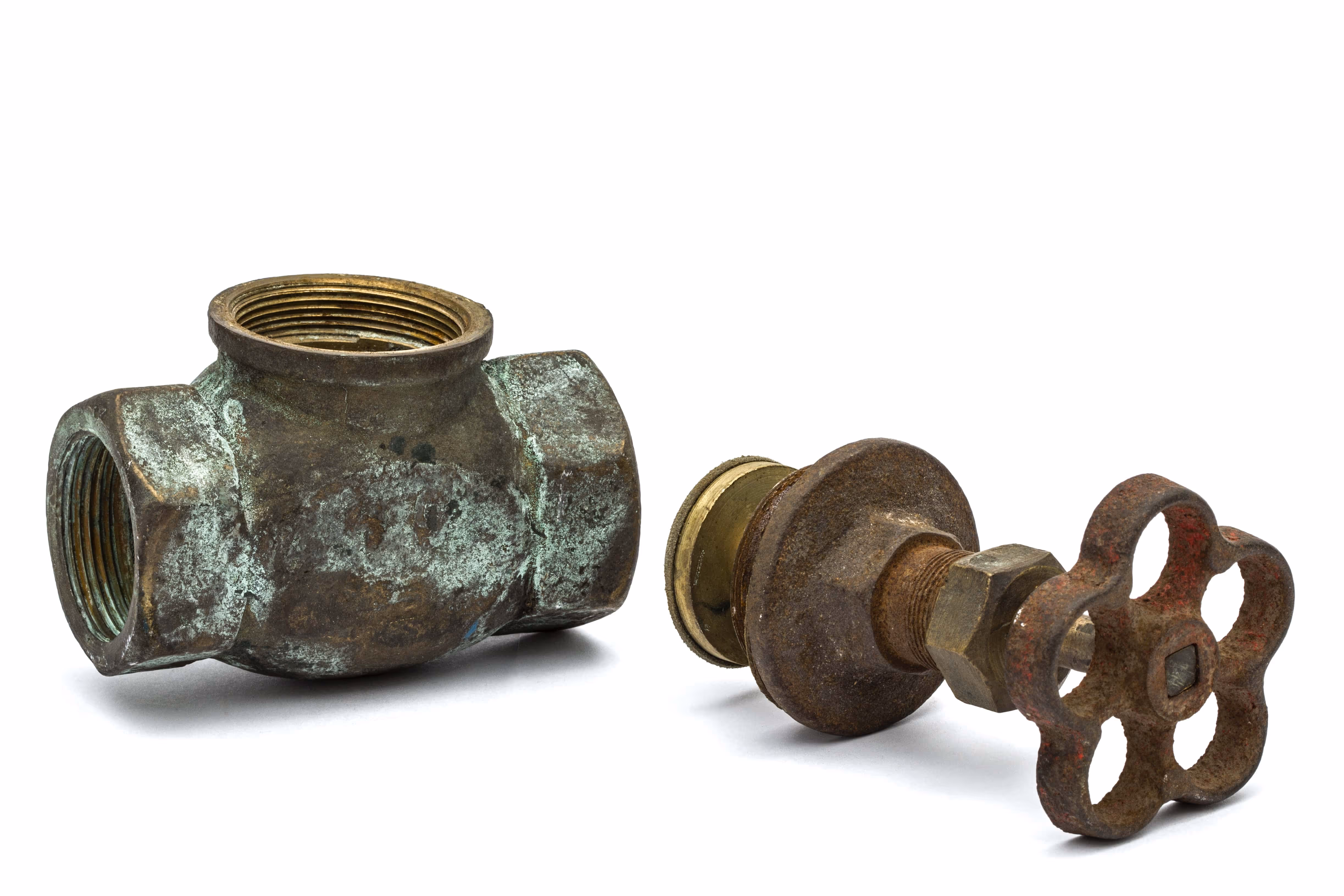 Two old, corroded plumbing valve components—one threaded check valve and one rusted gate valve with a flower-shaped handle—displayed on a white background.