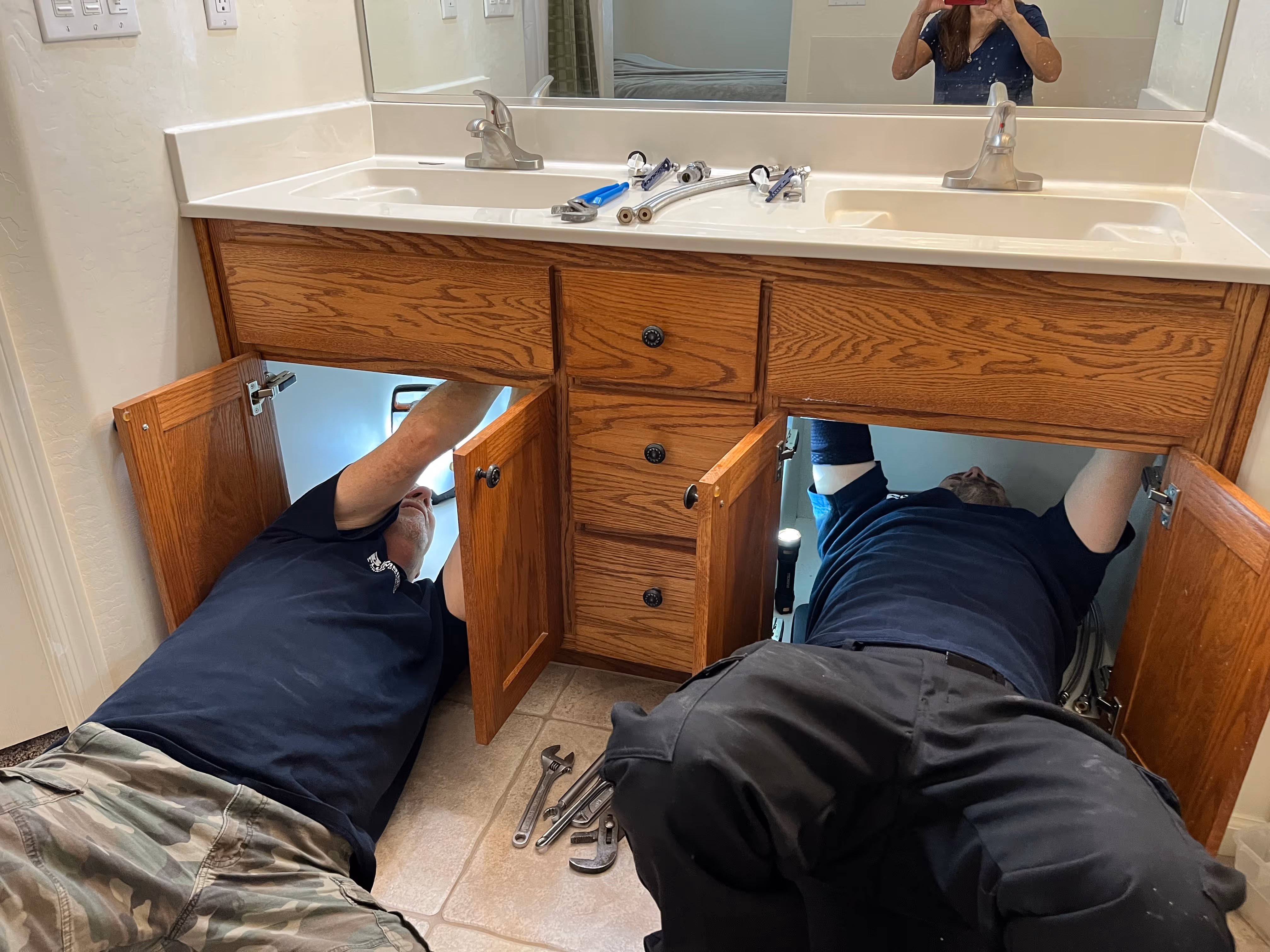 Two plumbers working on two bathroom sinks.