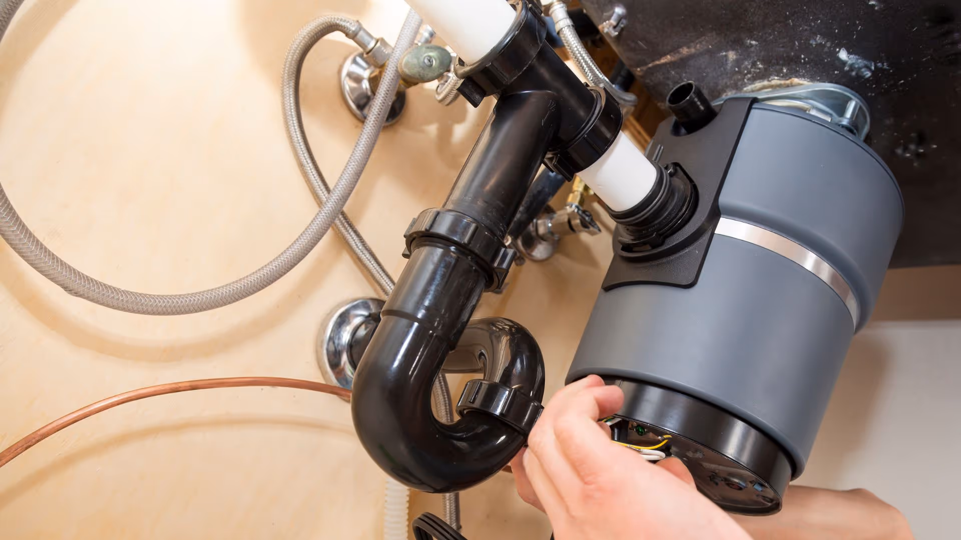 Two hands working on a garbage disposal.