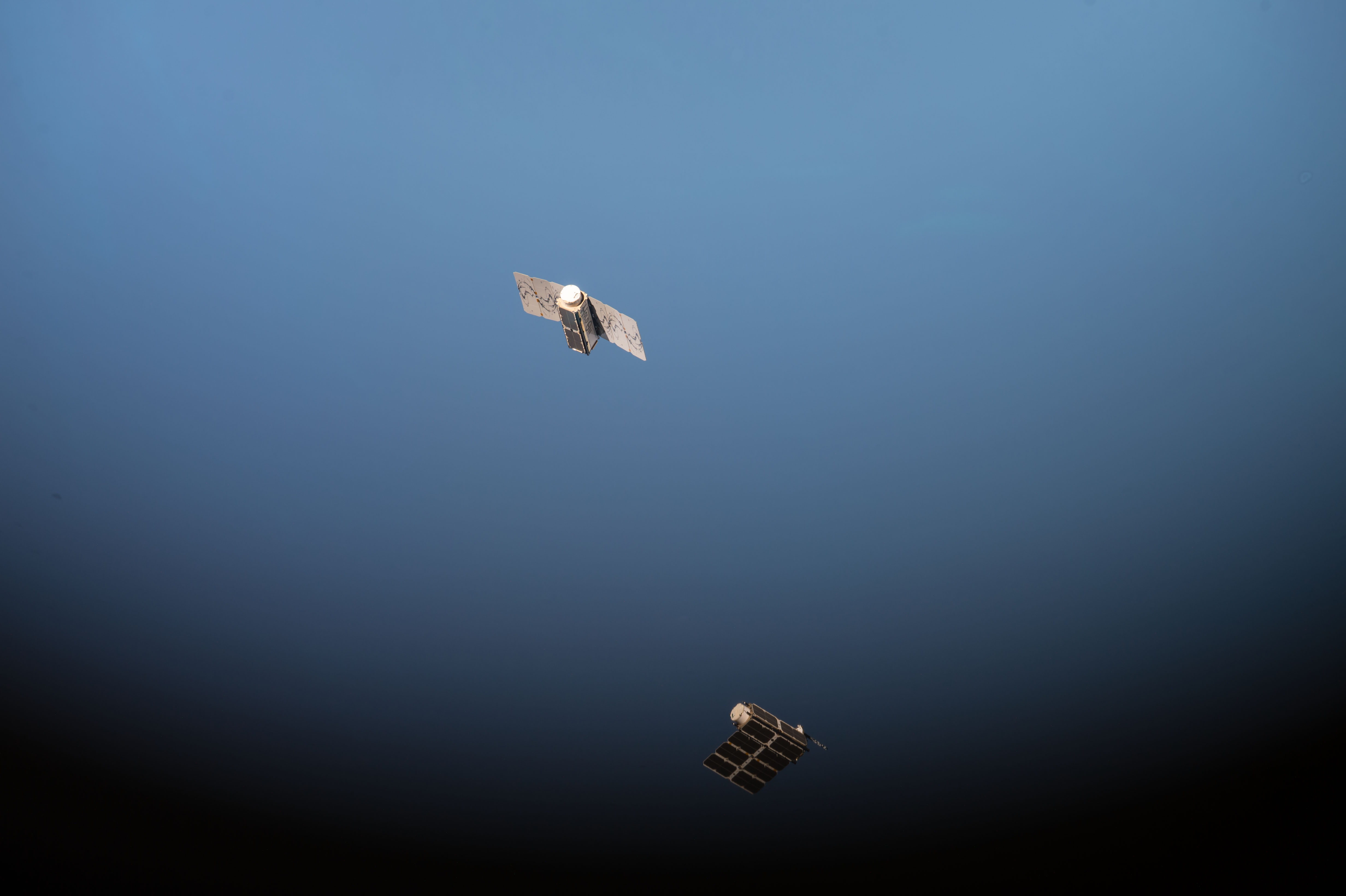 Two Planet Labs Dove CubeSat satellites floating in space after deployment from the International Space Station