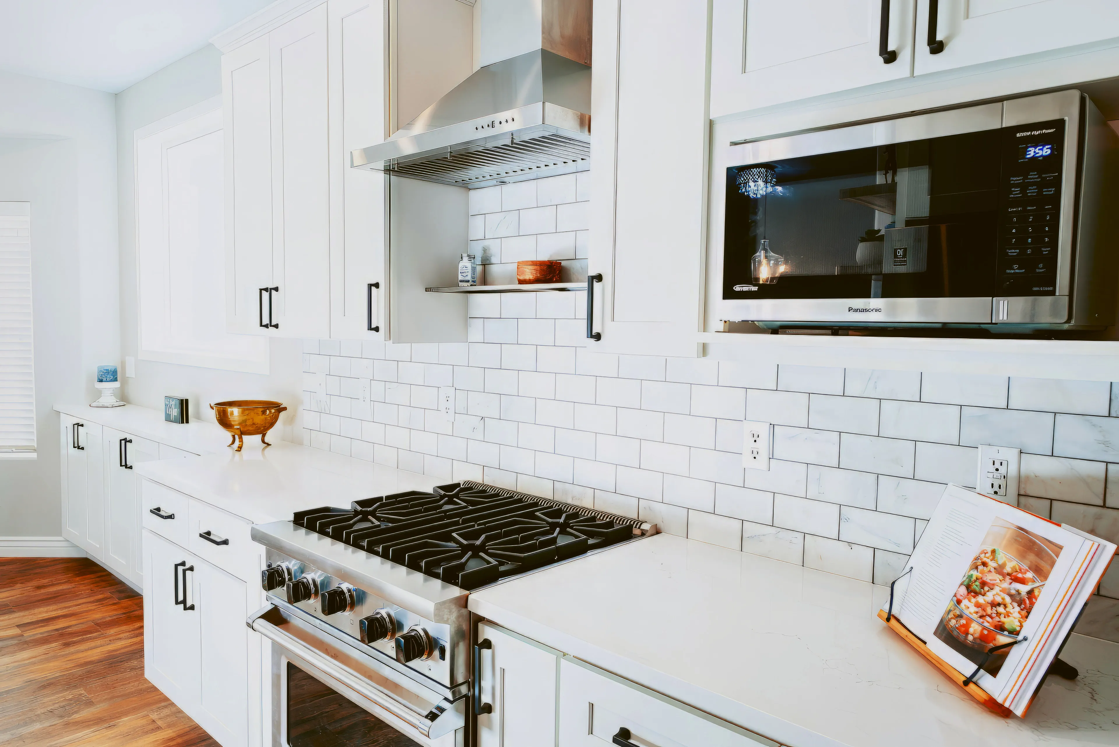 Modern kitchen with white cabinetry, marble subway tile backsplash, stainless steel stove and microwave, and wooden floor.