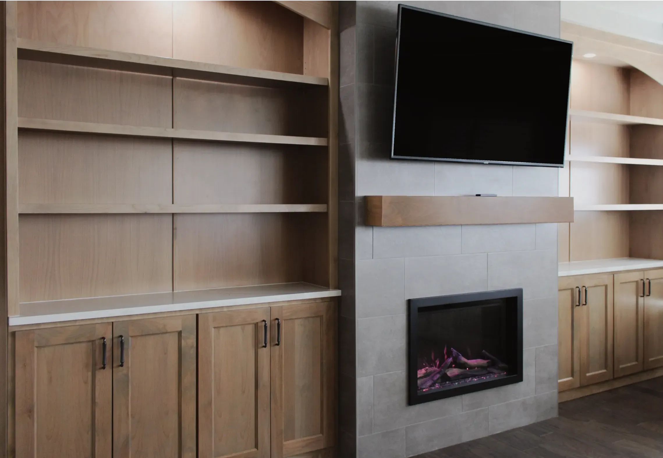 Modern living room with built-in wooden shelves and cabinets flanking a tiled fireplace topped by a mounted flat-screen TV.