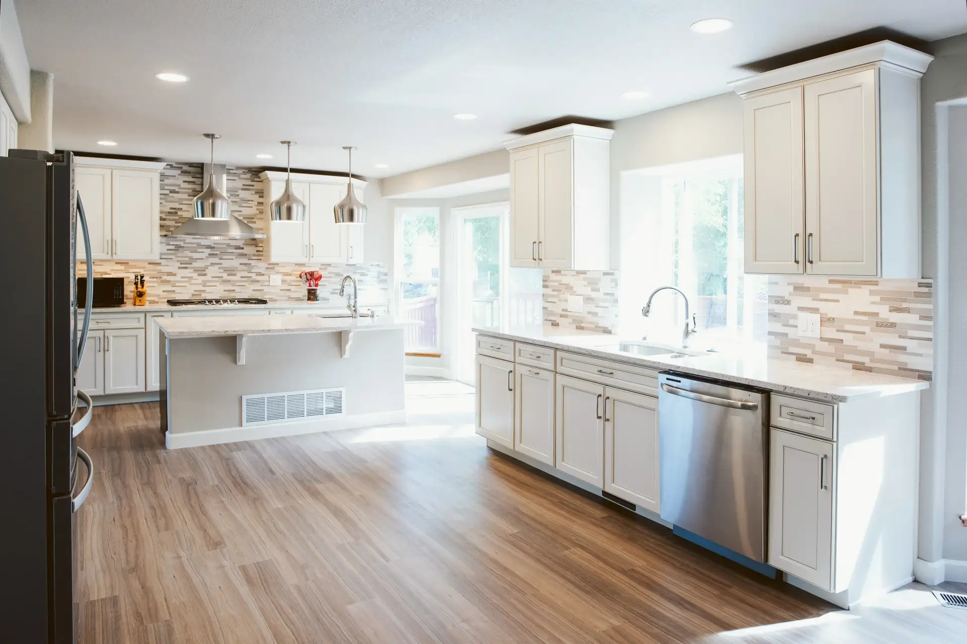 Bright modern kitchen with white cabinetry, stainless steel appliances, island with pendant lights, and wood-look flooring.