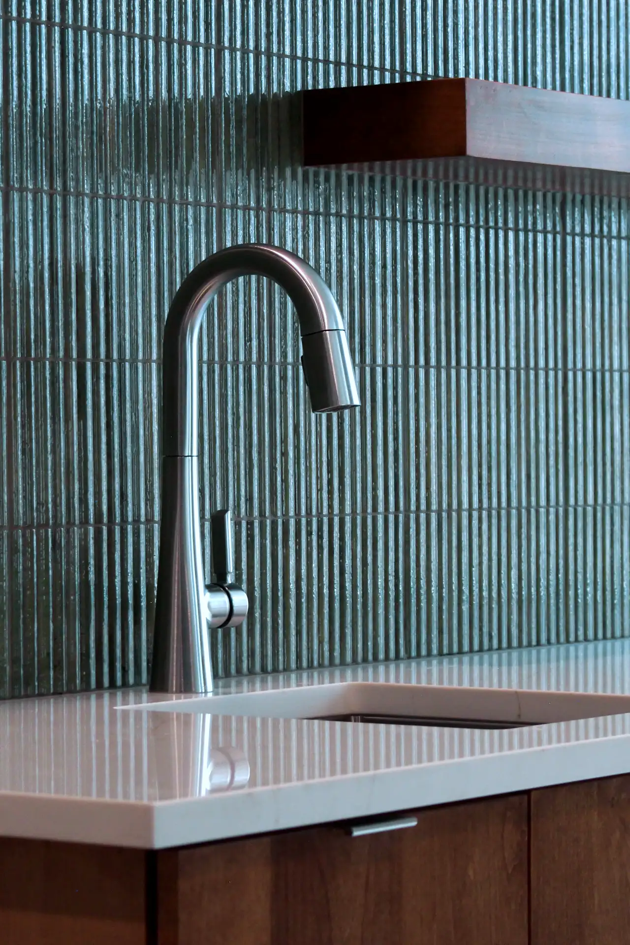 Modern stainless steel kitchen faucet with single lever on a white countertop and textured green tile backsplash.