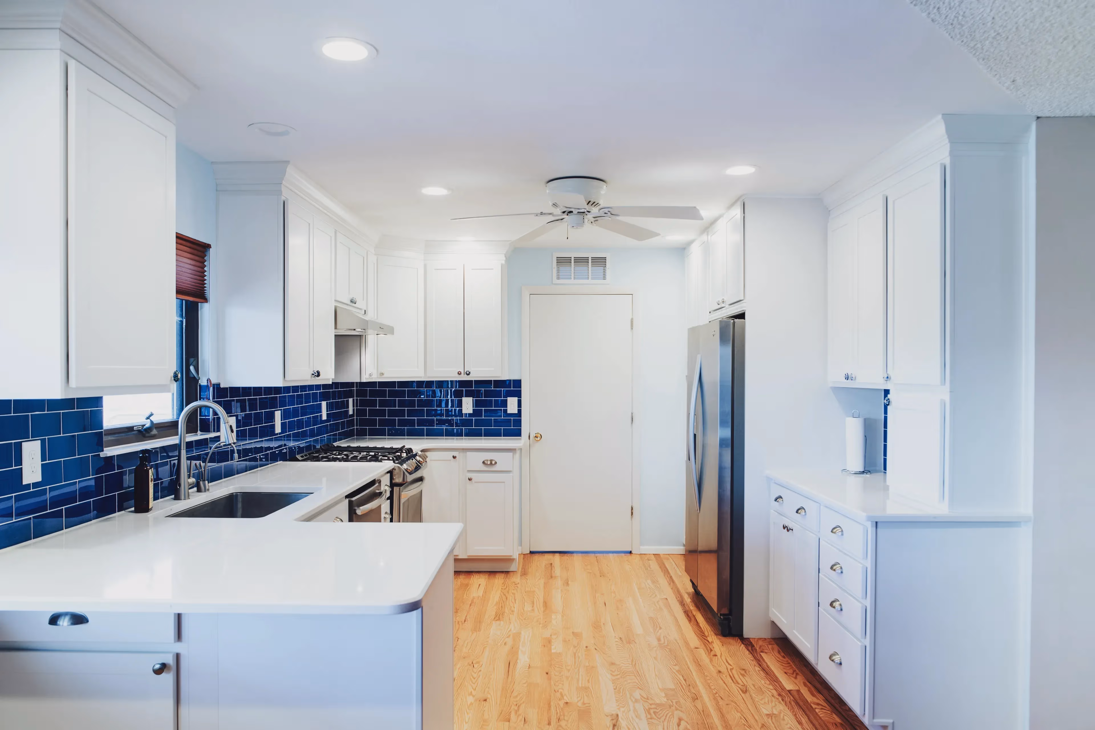 Modern kitchen with white cabinets, blue subway tile backsplash, stainless steel appliances, and light wood floor.