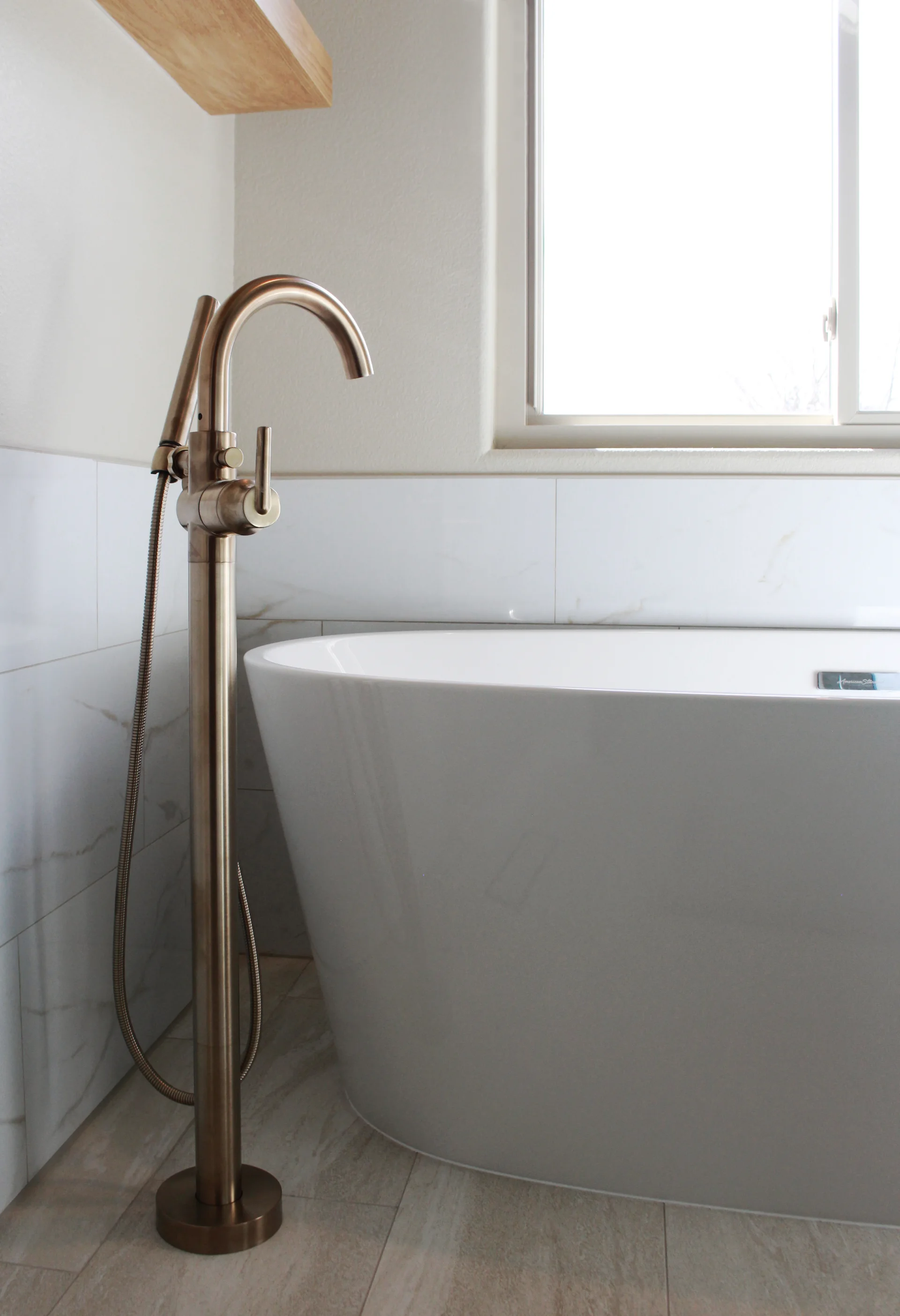 Modern bathroom with white freestanding bathtub and bronze-tone floor-mounted faucet next to window.