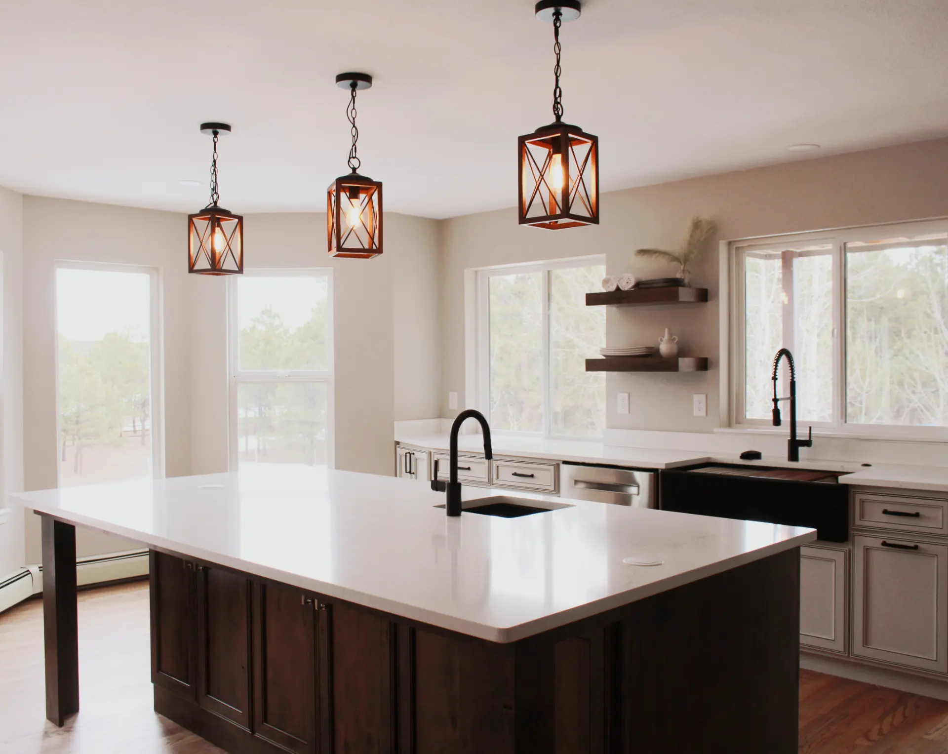Modern kitchen with a large white island countertop, dark wood cabinets, black sink faucets, three pendant lights, and multiple windows.