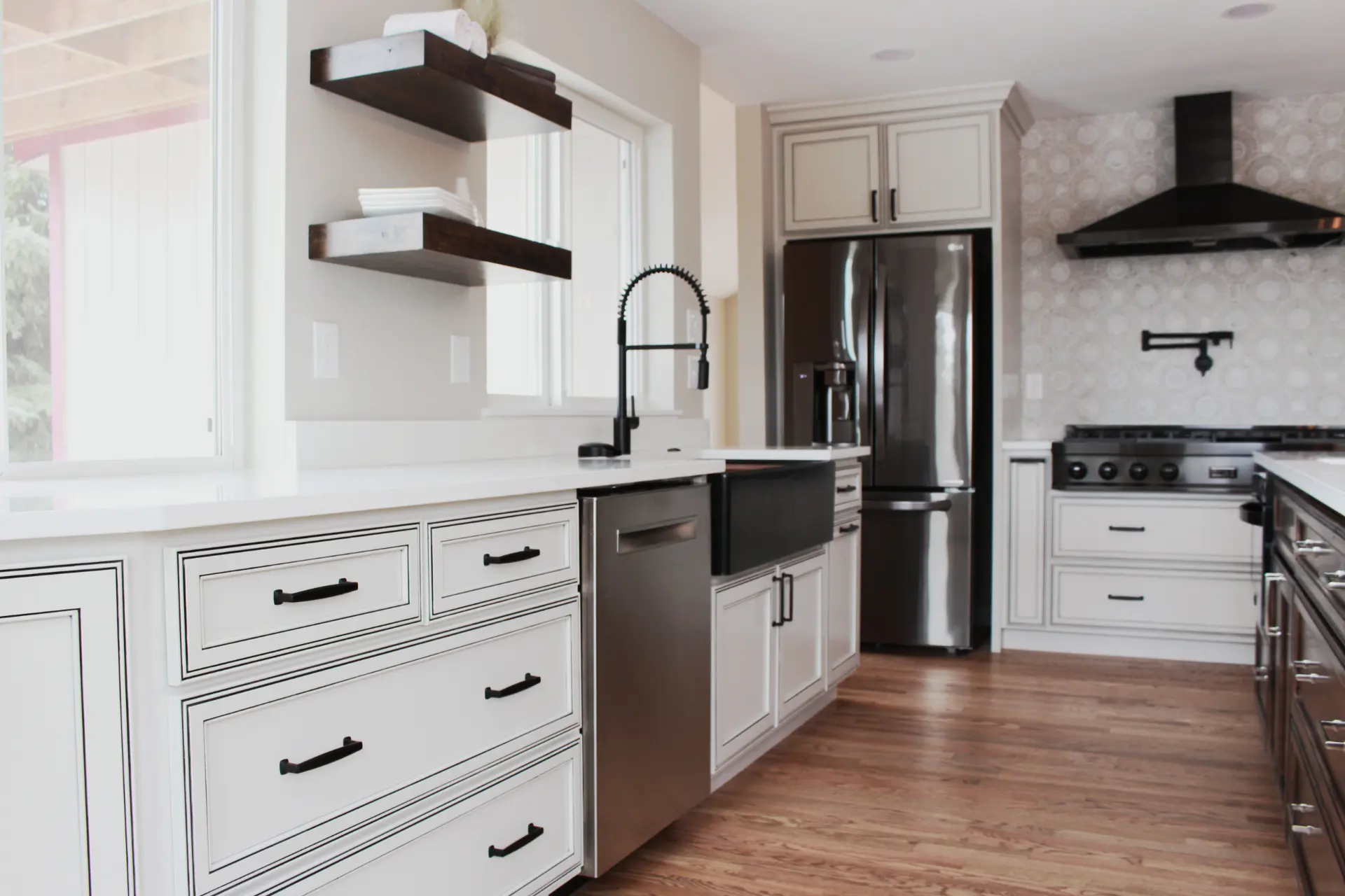 Bright modern kitchen with white cabinetry, stainless steel appliances, black farmhouse sink, and wooden floating shelves.